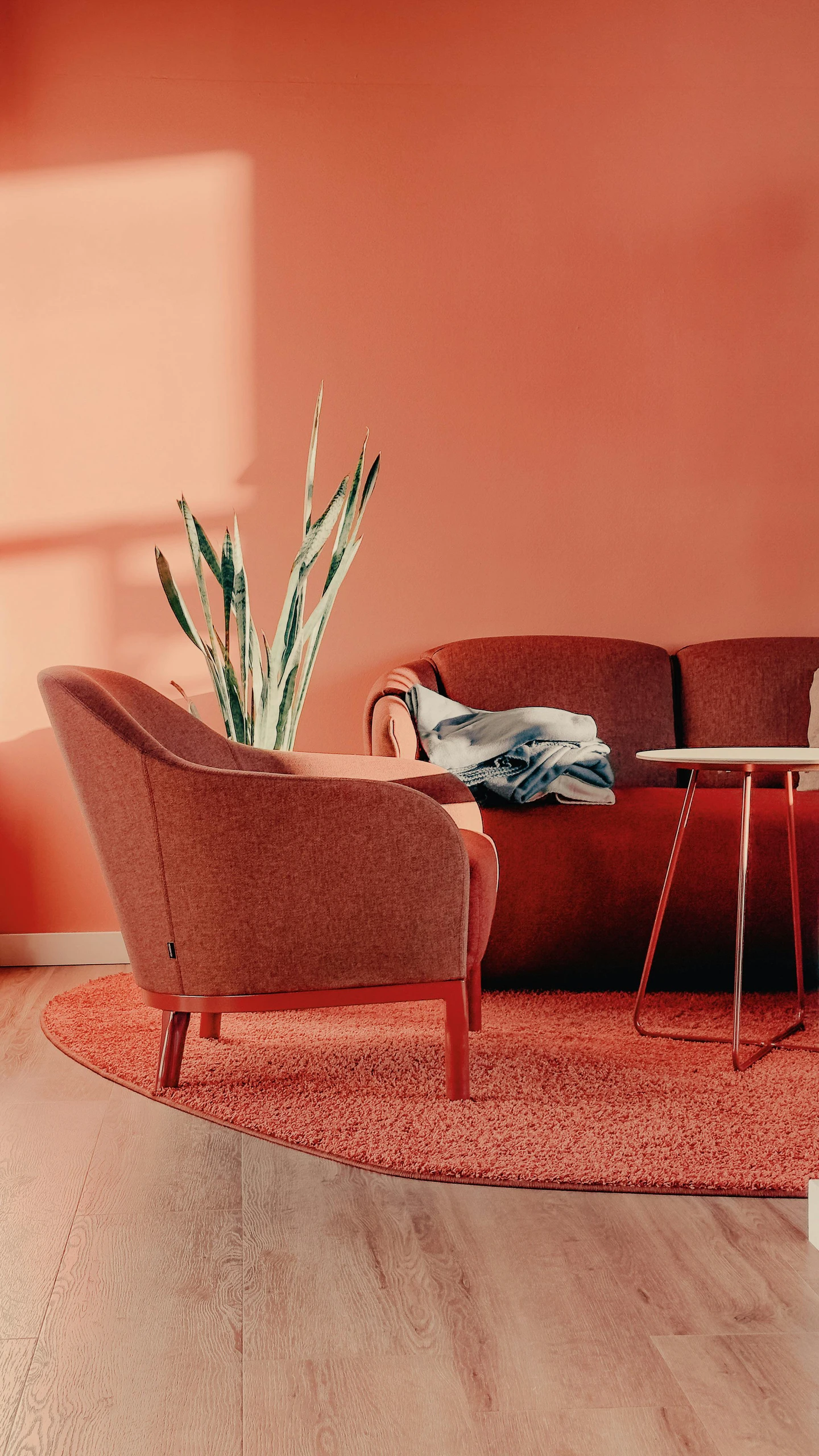 Stylish room corner showcasing a red accent wall with eye-catching color, complemented by a matching armchair, sofa, and rug. An inspiring example of small bedroom ideas with storage that incorporate bold wall colors for visual impact.