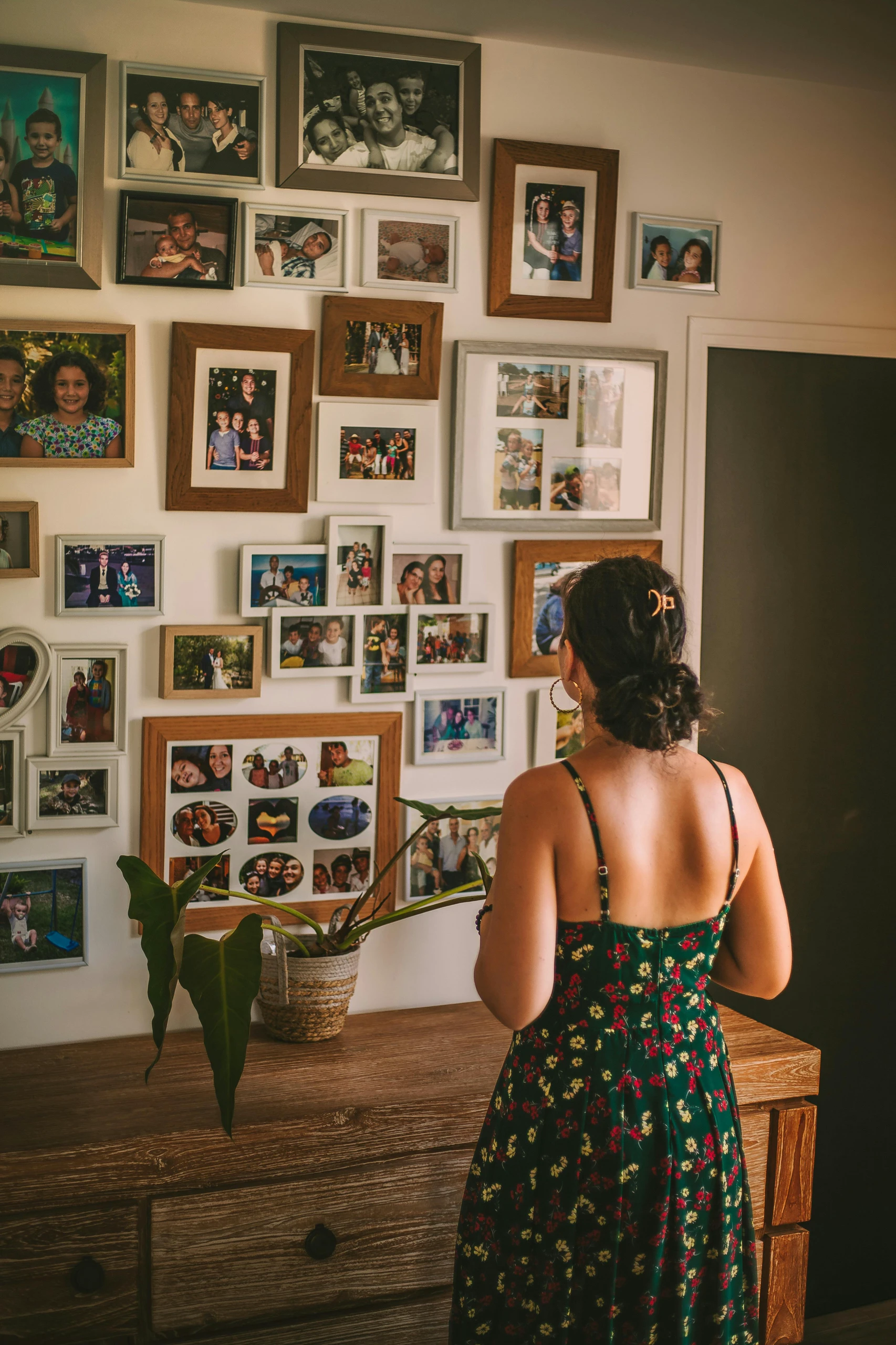 Woman standing in front of a family photo wall filled with assorted picture frames, showcasing a personal and heartwarming example of living room decor ideas for walls.