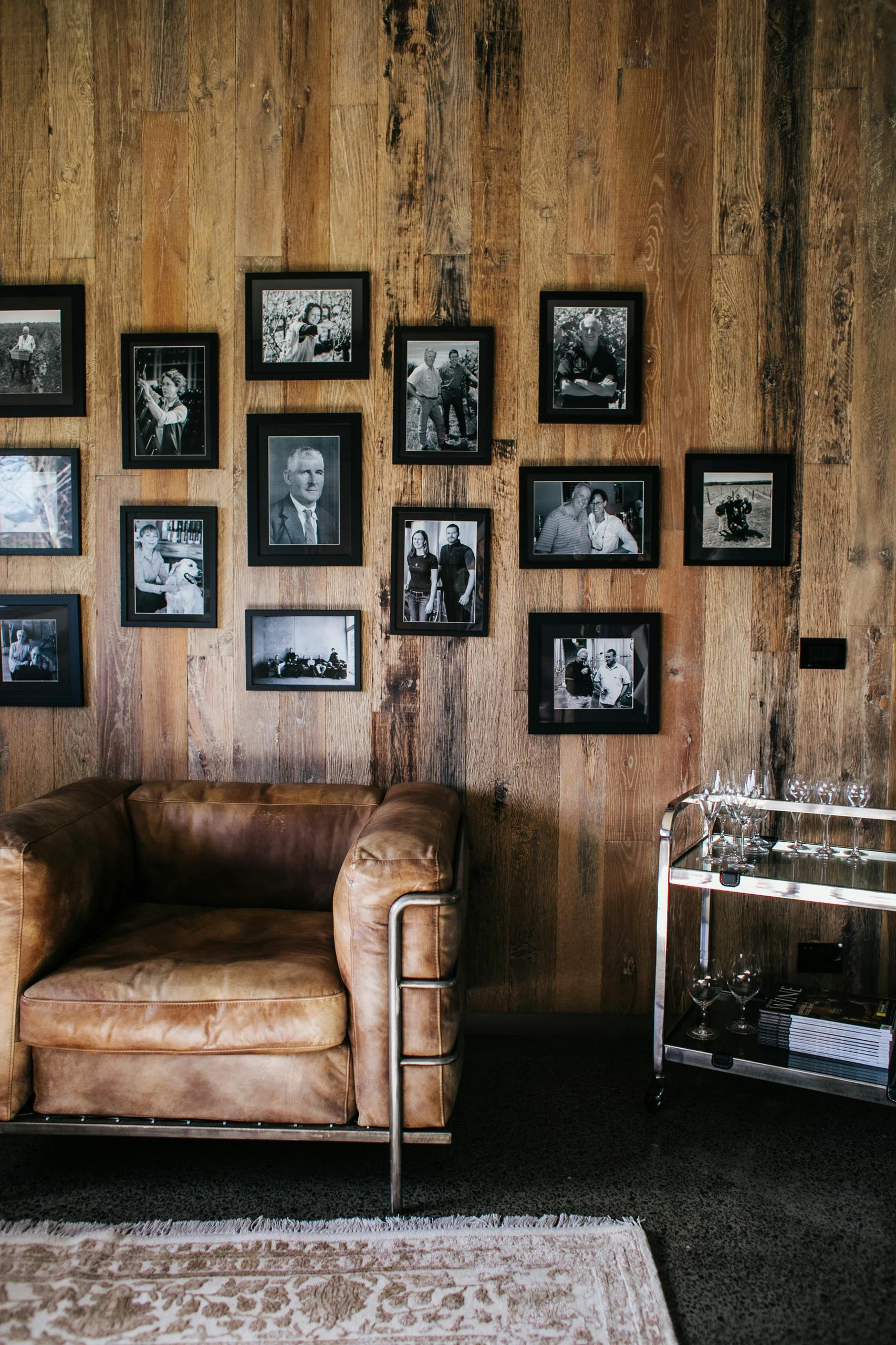 Rustic living space showcasing living room farmhouse decor ideas with a cozy leather armchair, wooden wall panels, and a striking family photo wall in black frames that adds warmth and personal charm to the room.