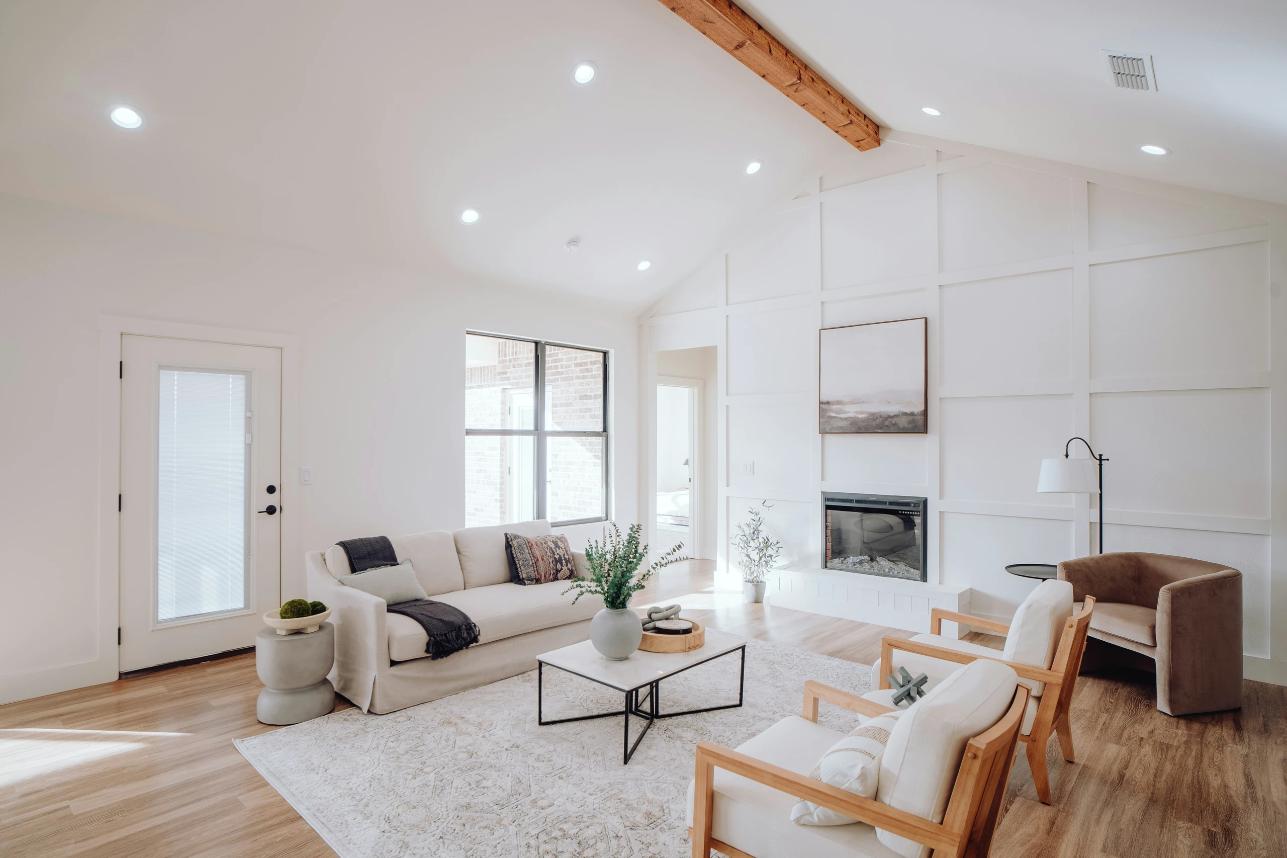 Bright and airy living room showcasing modern living room farmhouse decor ideas with neutral tones, wooden ceiling beam, and cozy farmhouse rugs that add warmth and texture to the space.