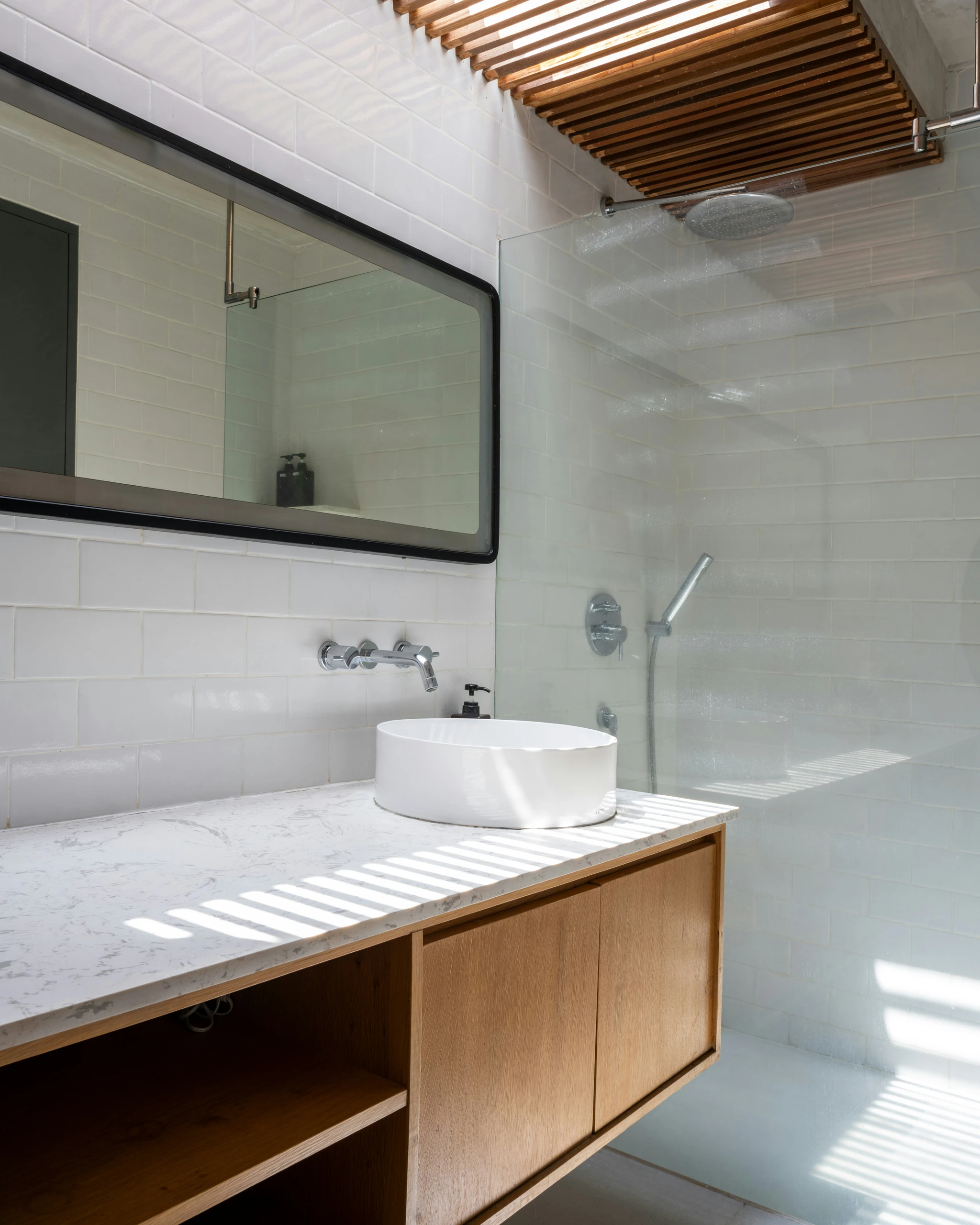 A bright and airy bathroom highlighting small bathroom ideas on a budget with a minimalistic design, featuring clean white tiles, a sleek floating vanity with open storage, and natural light streaming through wooden slats for a serene and uncluttered look.