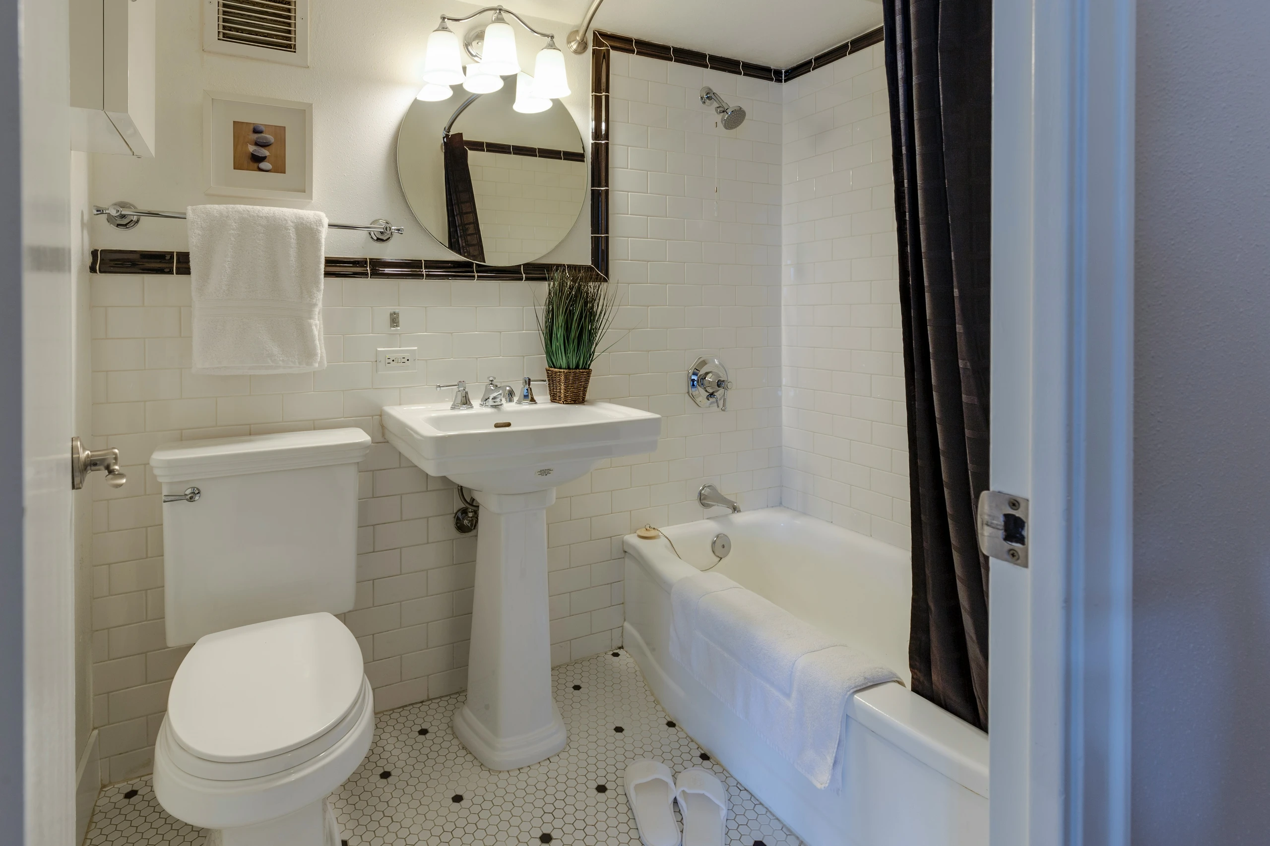A cozy and functional bathroom showcasing small bathroom ideas on a budget, featuring a compact layout with classic white tiles, a space-efficient bathtub, and a stylish pedestal-style small wash basin that maximizes floor space while maintaining a timeless look.