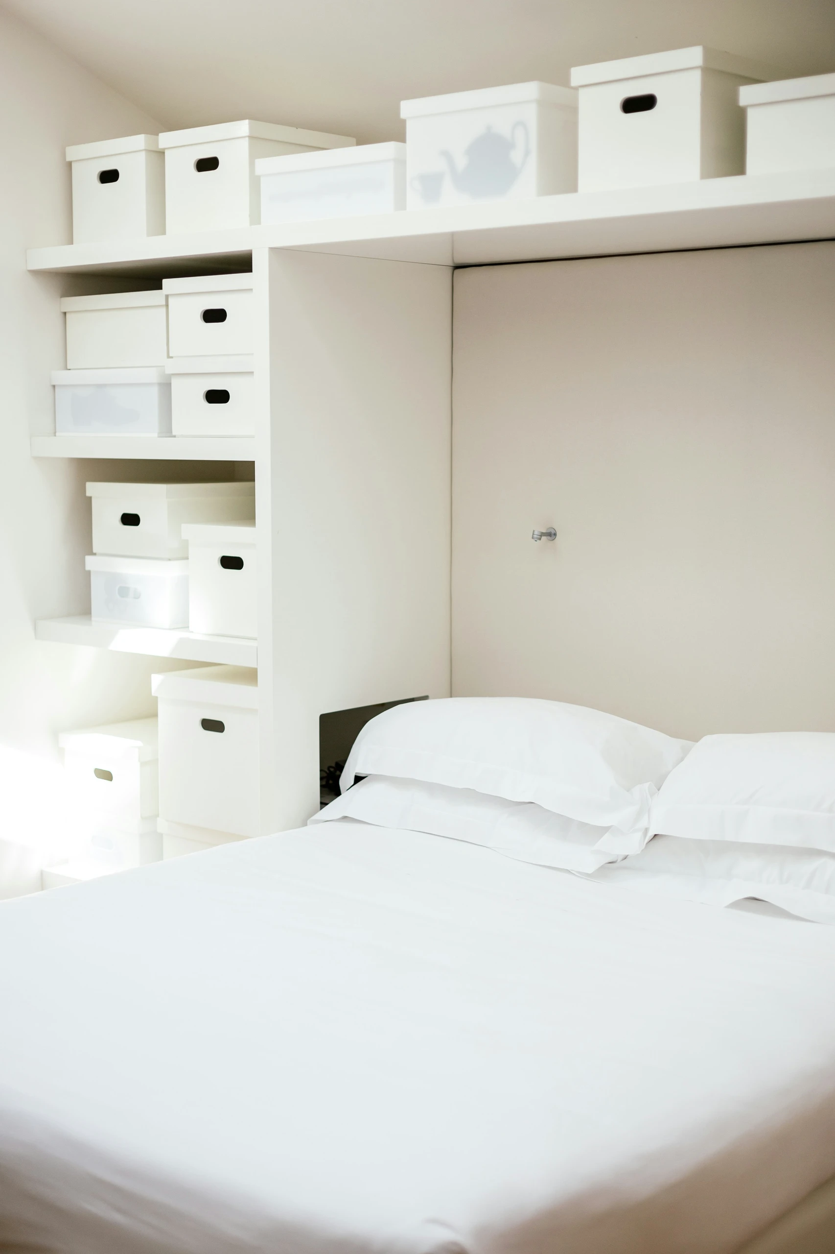Cozy bedroom with white bedding and built-in shelving filled with stackable boxes, showcasing clever small bedroom ideas with storage that maximize vertical space while maintaining a clean, minimalist look.