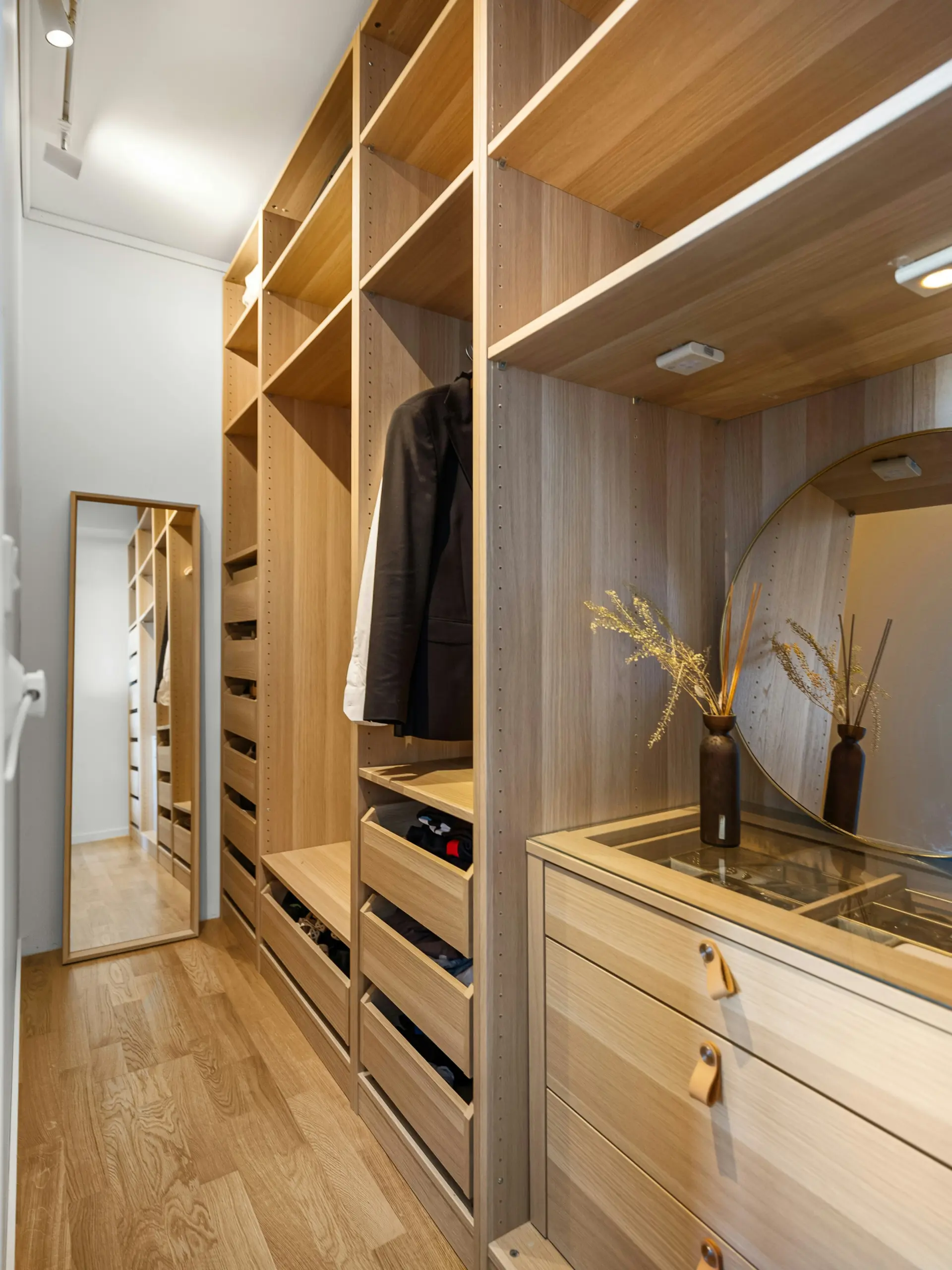A sleek and space-saving example of small bedroom ideas with storage, this image features custom built-in wardrobes in a narrow dressing area. The wooden units include open shelves, drawers, and hanging space, along with a vanity section and mirror, offering a seamless and organized solution for maximizing vertical and horizontal storage.
