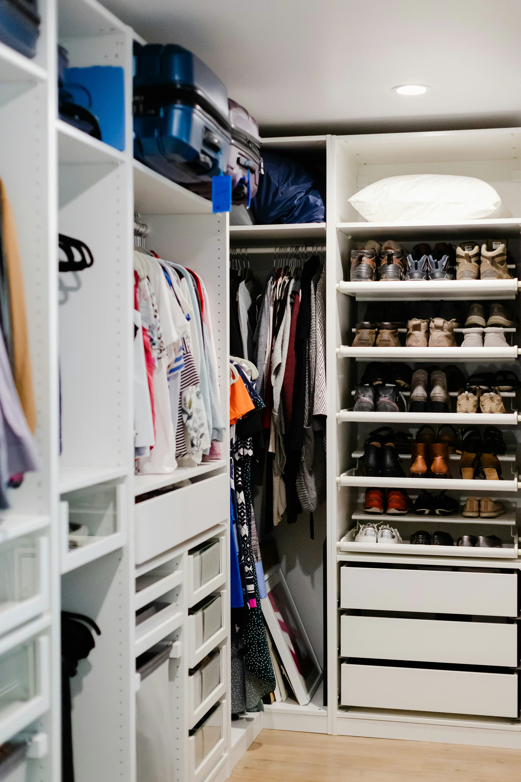 A highly efficient storage solution showcasing small bedroom ideas with storage, this image features custom closet organizers with shelves, drawers, and hanging space. Shoes, clothing, and suitcases are neatly arranged in a white built-in system, making the most of vertical space while keeping everything easily accessible and organized.