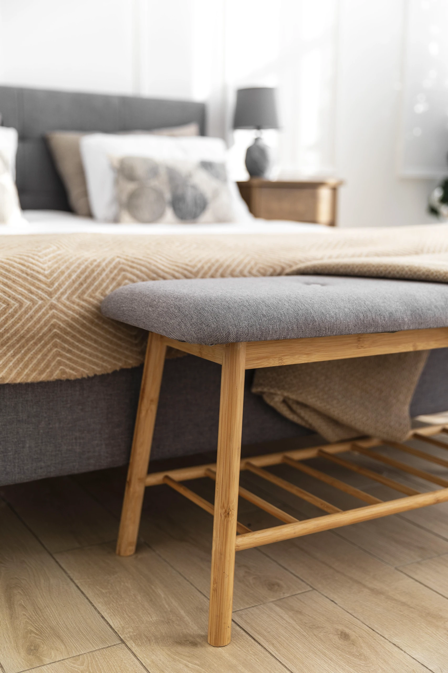 Close-up of a cozy bedroom featuring a padded bench with a wooden shelf at the foot of the bed, showcasing multi-functional furniture as part of small bedroom ideas with storage.