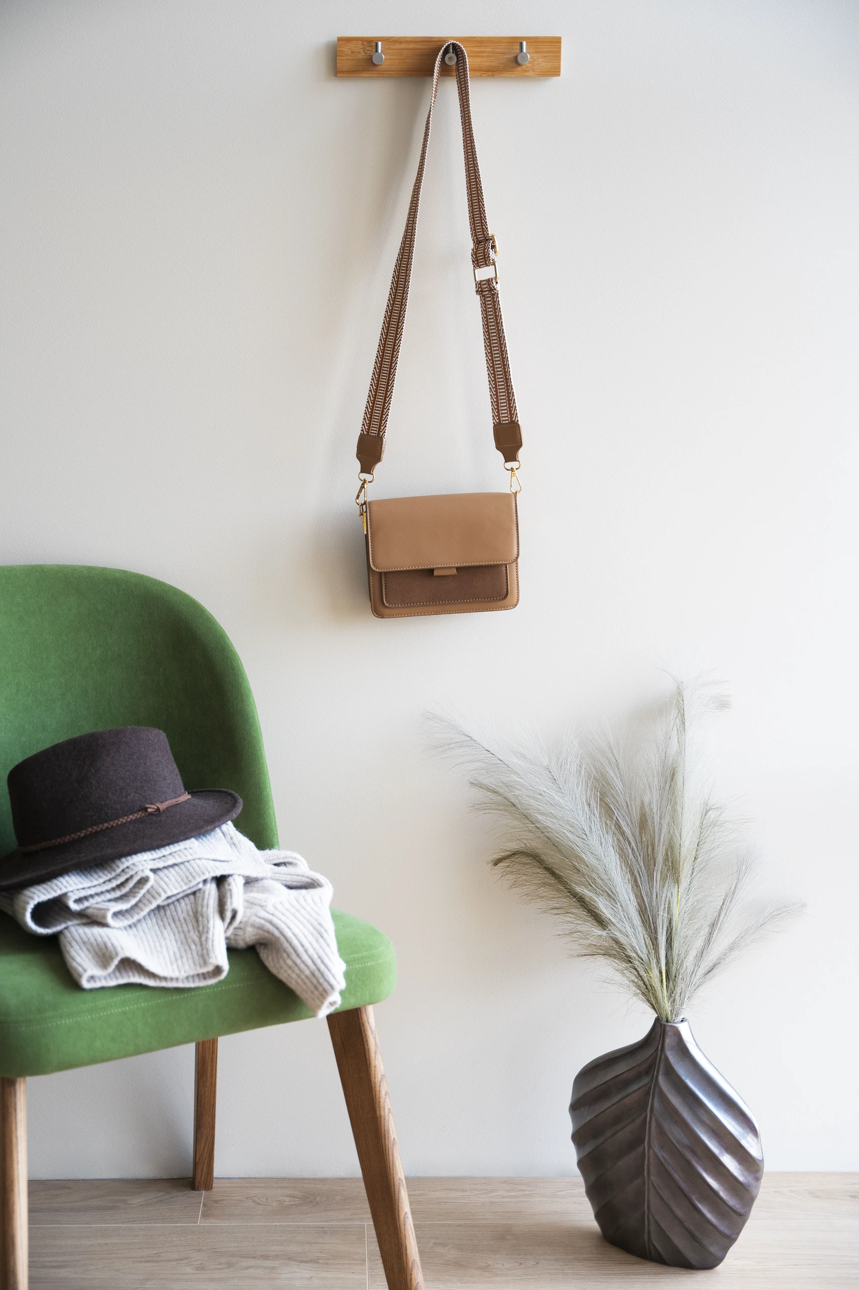 Alt text: Minimalist small bedroom setup showcasing clever storage solutions, featuring hooks on the wall used to hang a stylish handbag, a green chair with neatly folded clothes and a hat, and a decorative vase. An inspiring example of small bedroom ideas with storage that combine practicality and elegance.