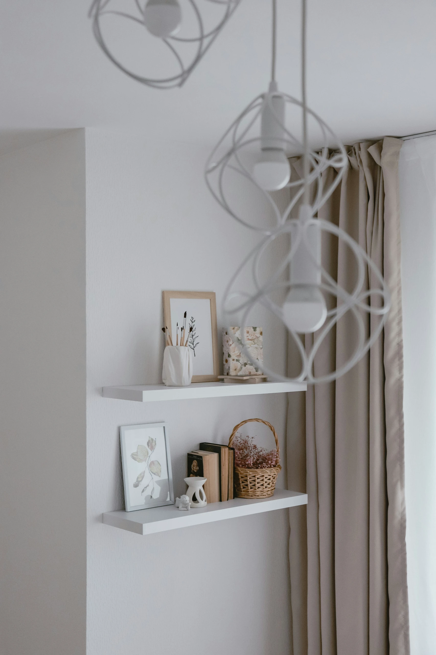 A bright and airy corner displaying small bedroom ideas with storage, featuring minimalist wall-mounted shelves. The two floating shelves hold framed artwork, books, a small basket, and decorative accents, offering a stylish way to organize and personalize vertical space in a compact room.