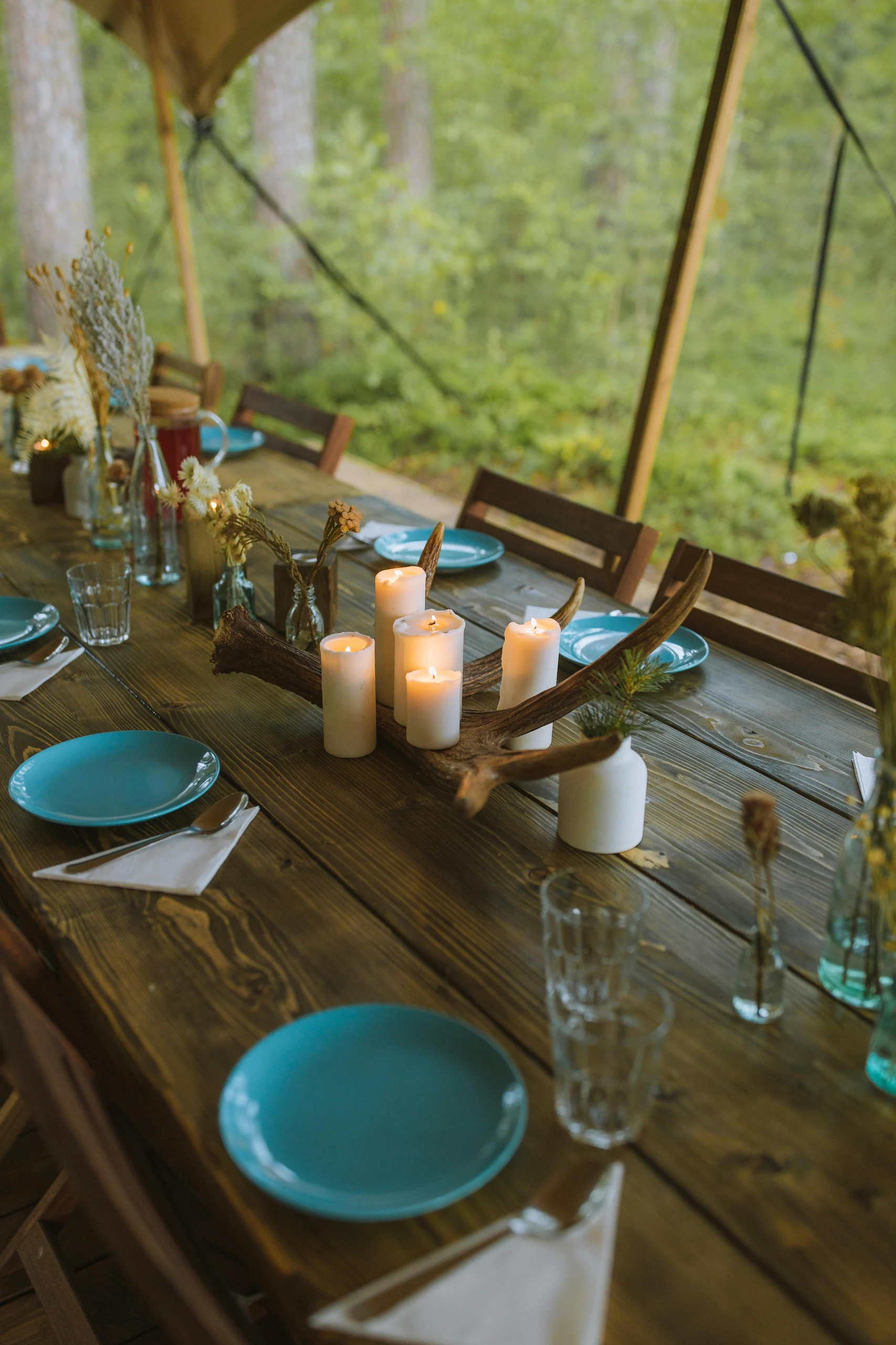Dining table centerpiece ideas featuring candles with different height arranged on a rustic wooden table, complemented by natural elements like antlers and dried flowers.