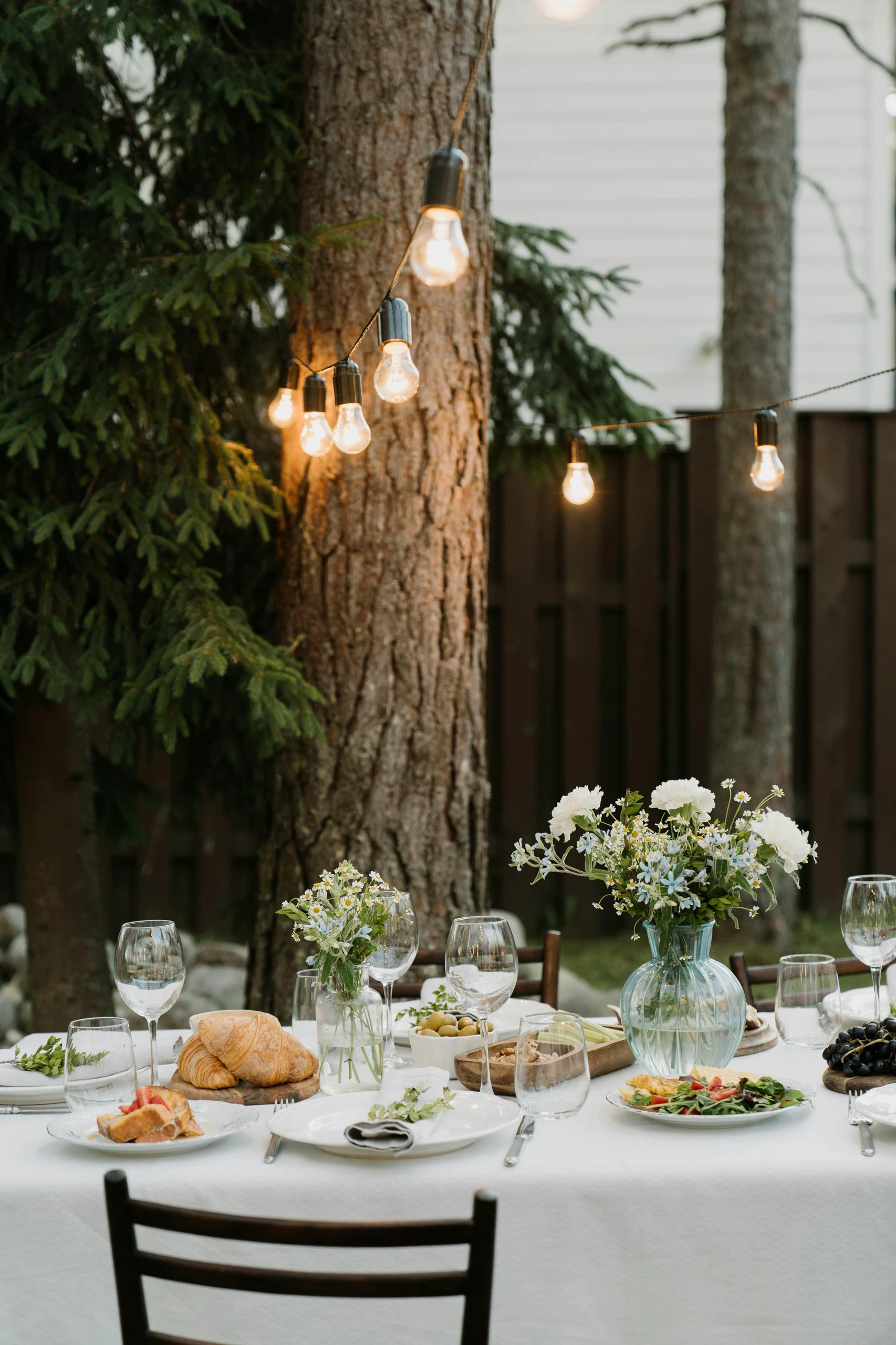 Dining table centerpiece ideas with a charming outdoor setup, featuring a glass vase of fresh wildflowers and soft fairy lights strung through trees, creating a cozy and inviting atmosphere.