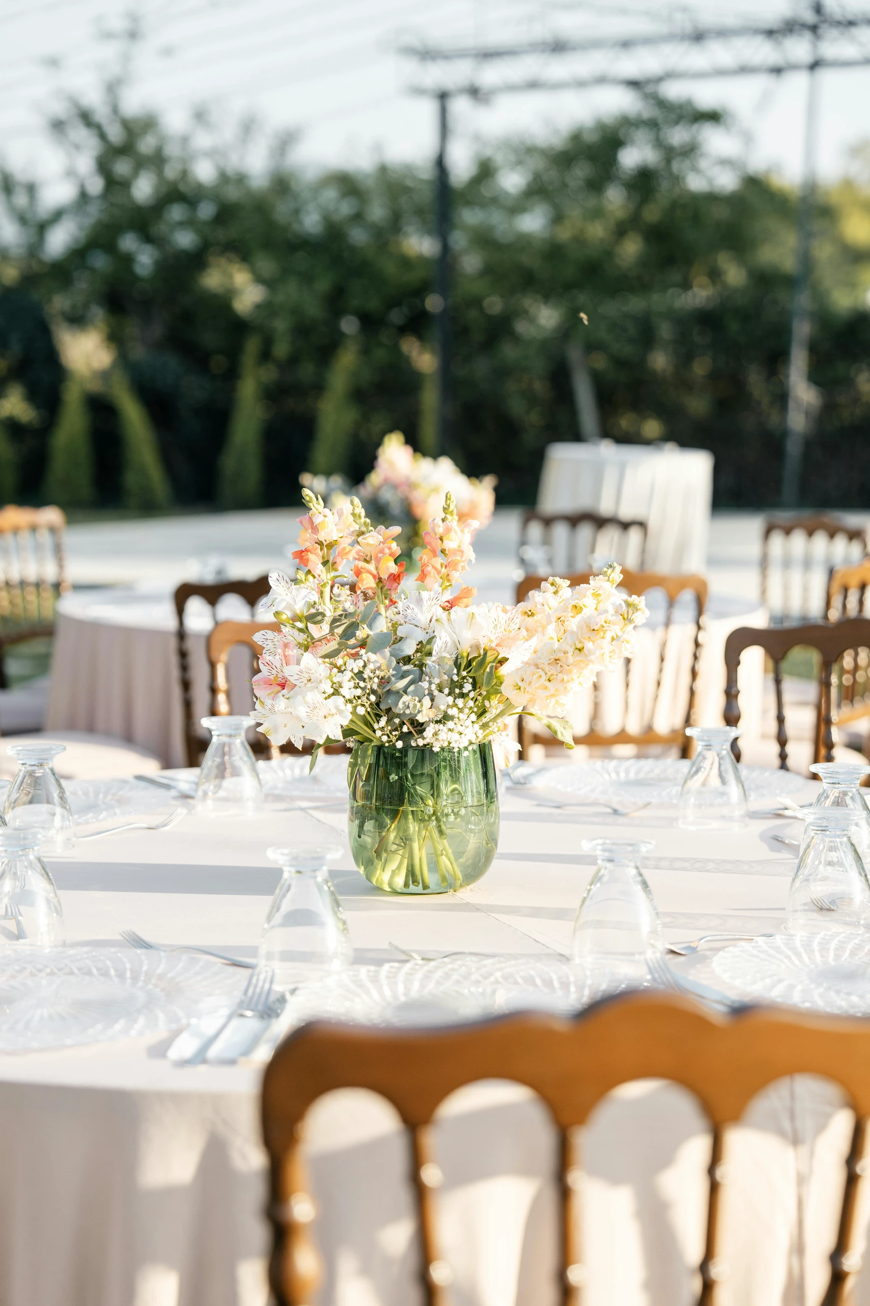Round outdoor dining table with a stylish centerpiece featuring fresh flowers in a green glass vase, showcasing elegant dining table centerpiece ideas perfect for events or gatherings.