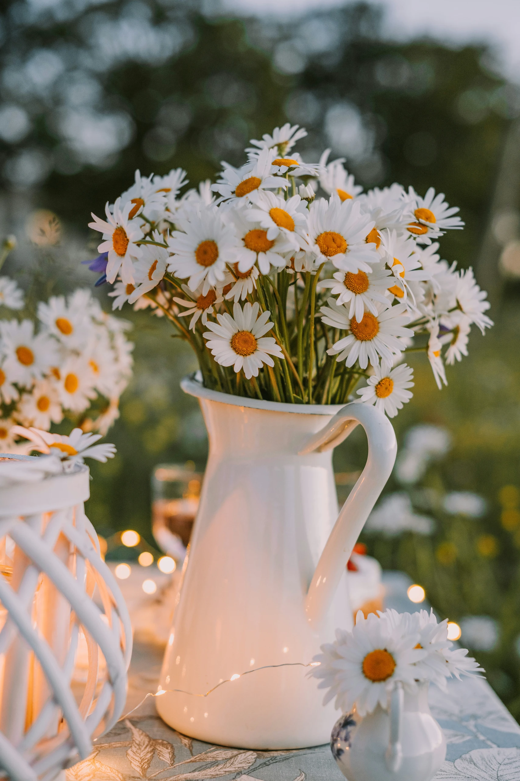 Charming dining table centerpiece ideas featuring a white jug filled with fresh daisies, creating a romantic and rustic outdoor table setting.
