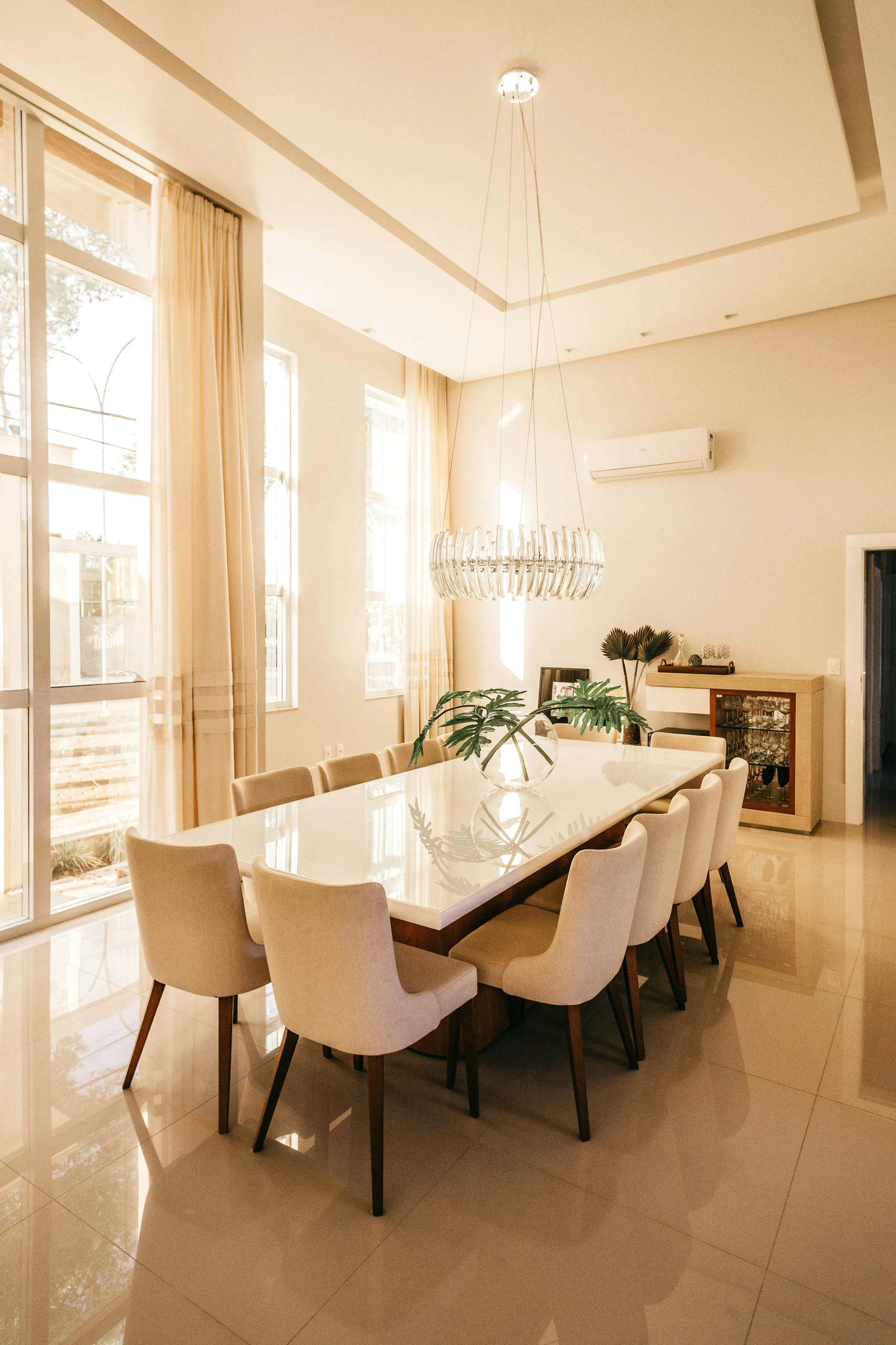 Elegant dining table centerpiece ideas for a minimalistic dining table, featuring a clear glass vase with simple green leaves in a bright, modern dining room with cream chairs and natural light.