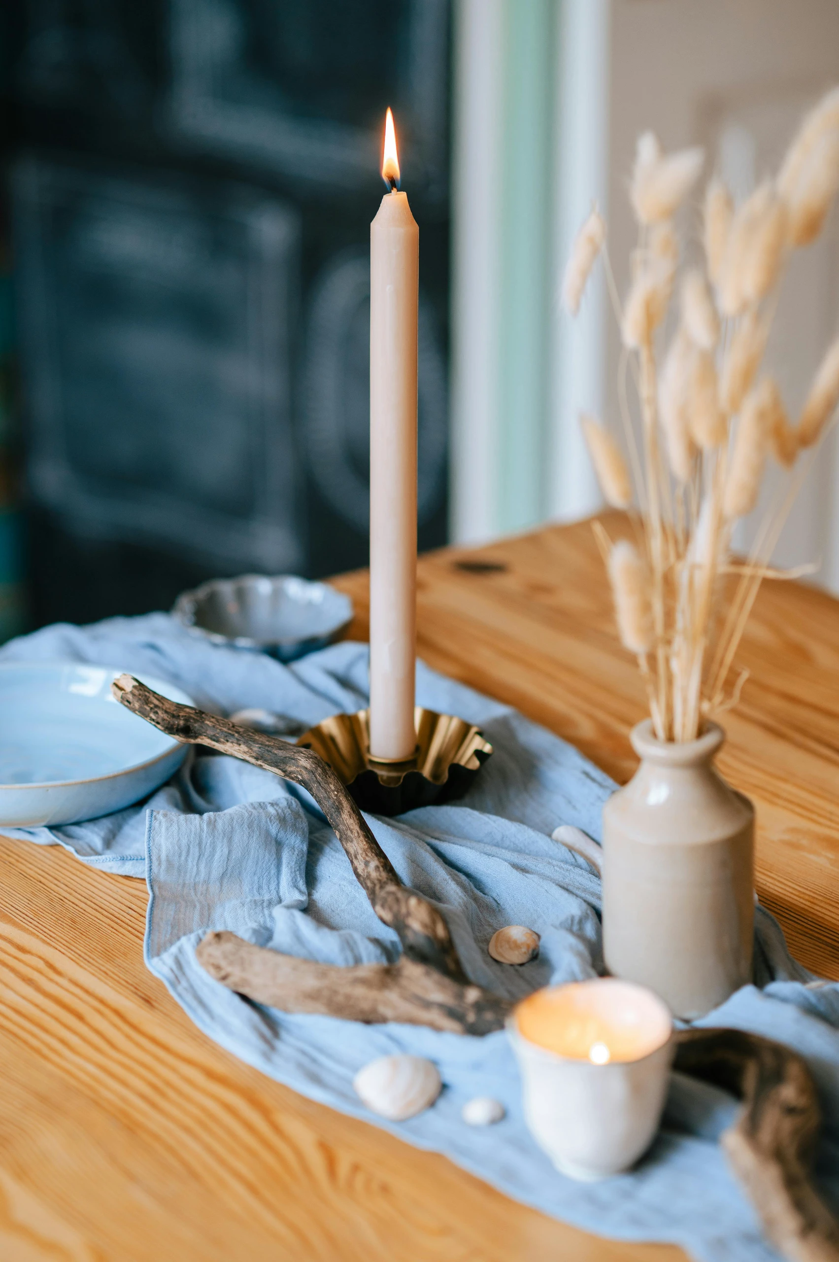 Dining table centerpiece ideas featuring a natural look with driftwood, candles, and dried flowers arranged on a soft blue fabric runner for a cozy, rustic feel.
