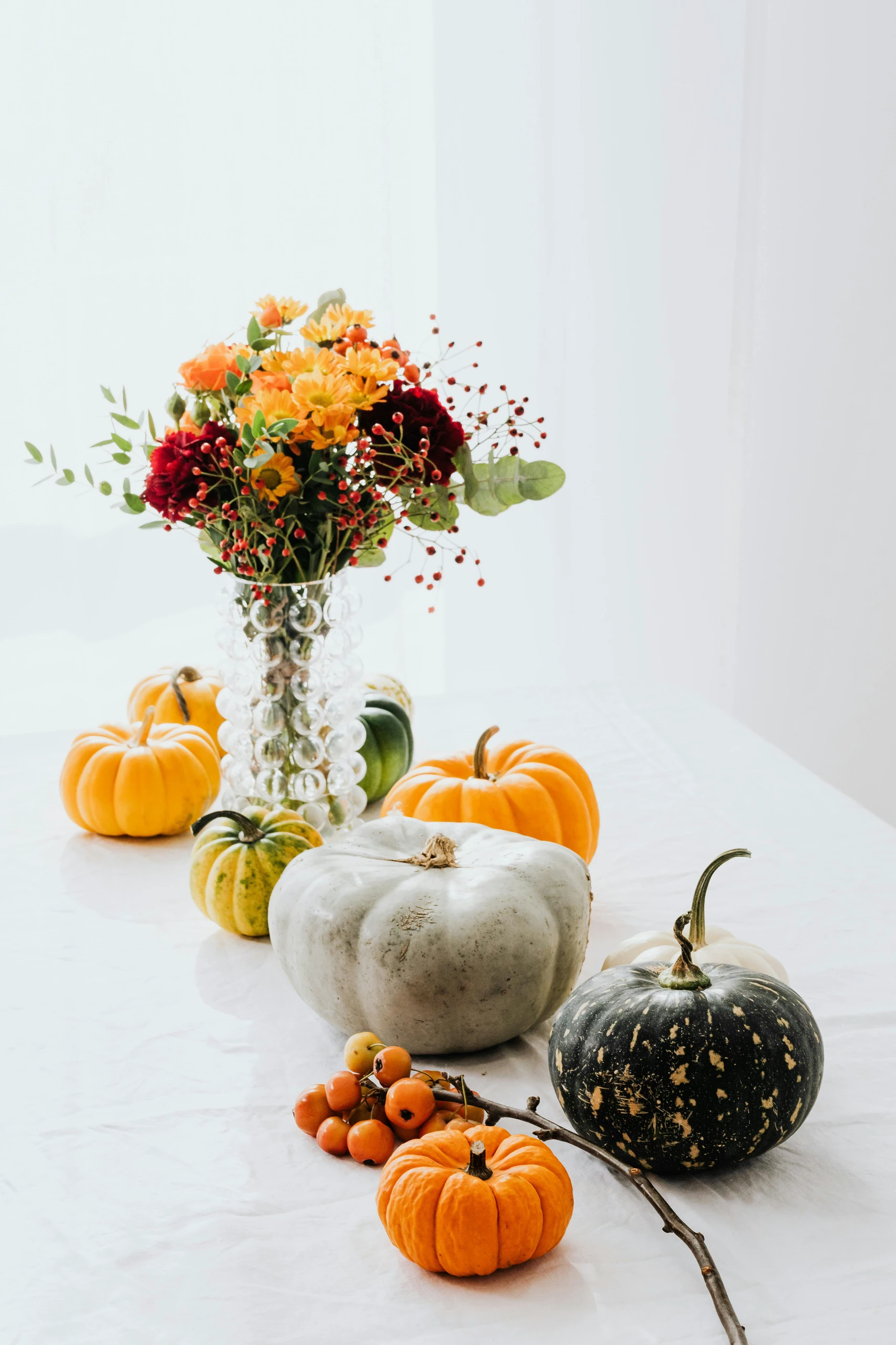 Creative dining table centerpiece ideas featuring a vibrant fall arrangement with pumpkins of various colors and sizes, paired with a clear glass vase filled with seasonal flowers and berries.