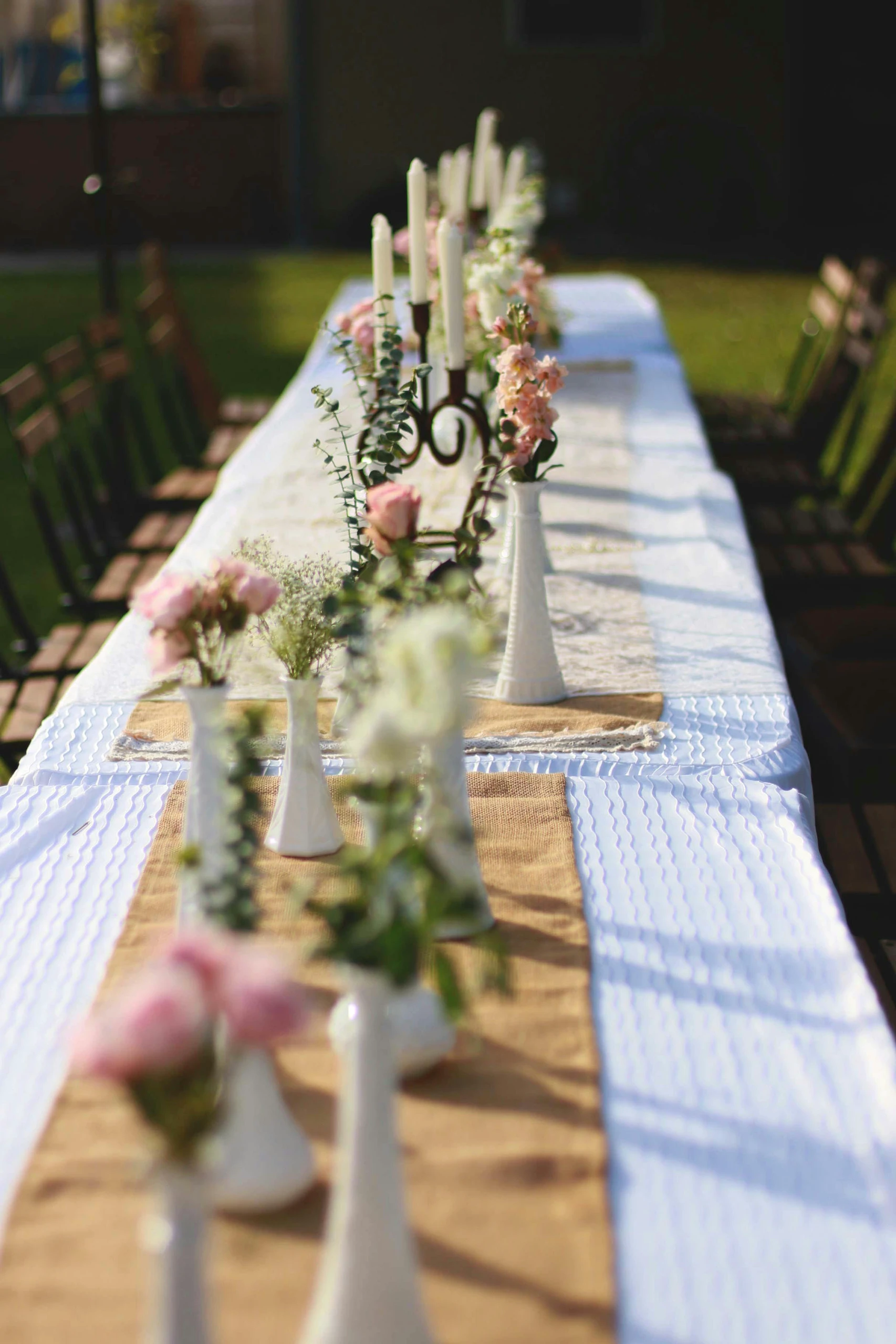 Charming outdoor dining setup featuring a row of many small vases with fresh flowers and candles, showcasing creative dining table centerpiece ideas for elegant gatherings.