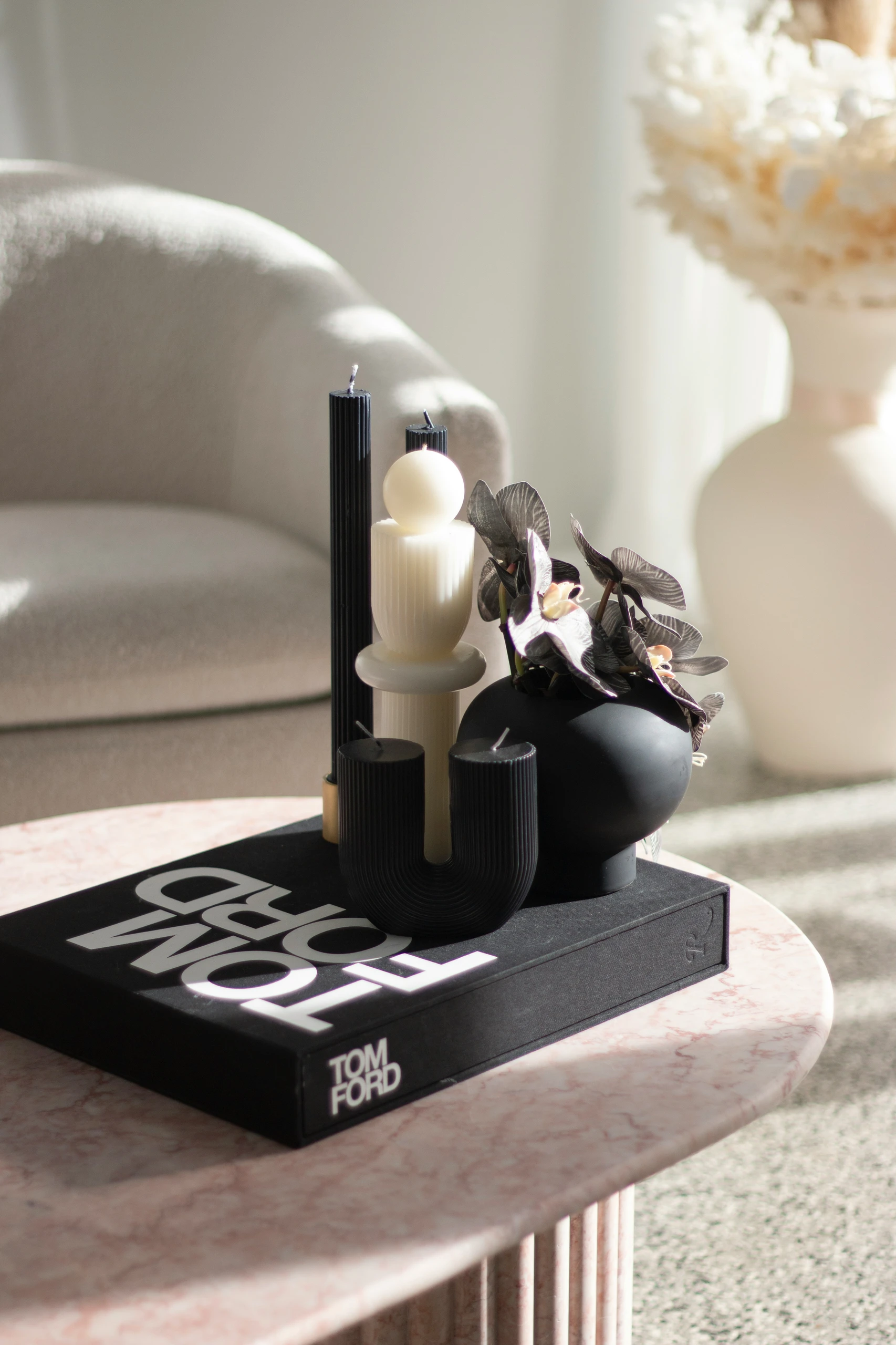 A stylish example of how to decorate a round coffee table with black and white coffee table decor, featuring sculptural candles, a matte black vase with dark flowers, and a bold Tom Ford book as a base. Perfect for modern, minimalist, or monochrome interiors.
