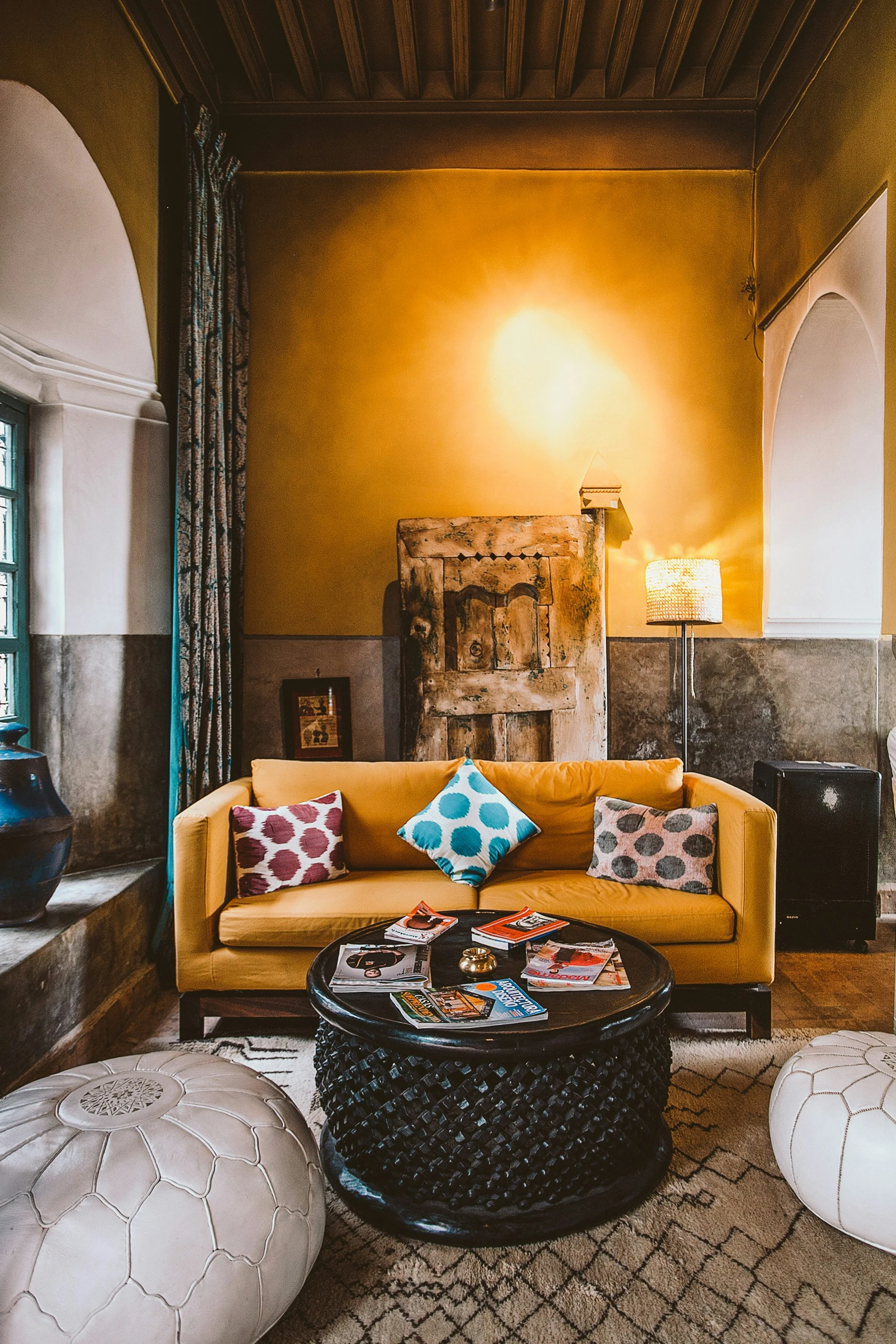 A vibrant living room showing how to decorate a round coffee table with magazines for a casual, welcoming look. The carved black coffee table becomes a stylish focal point, offering a versatile surface for reading materials, a small gold decor accent, and informal entertaining in a colorful, character-filled space.