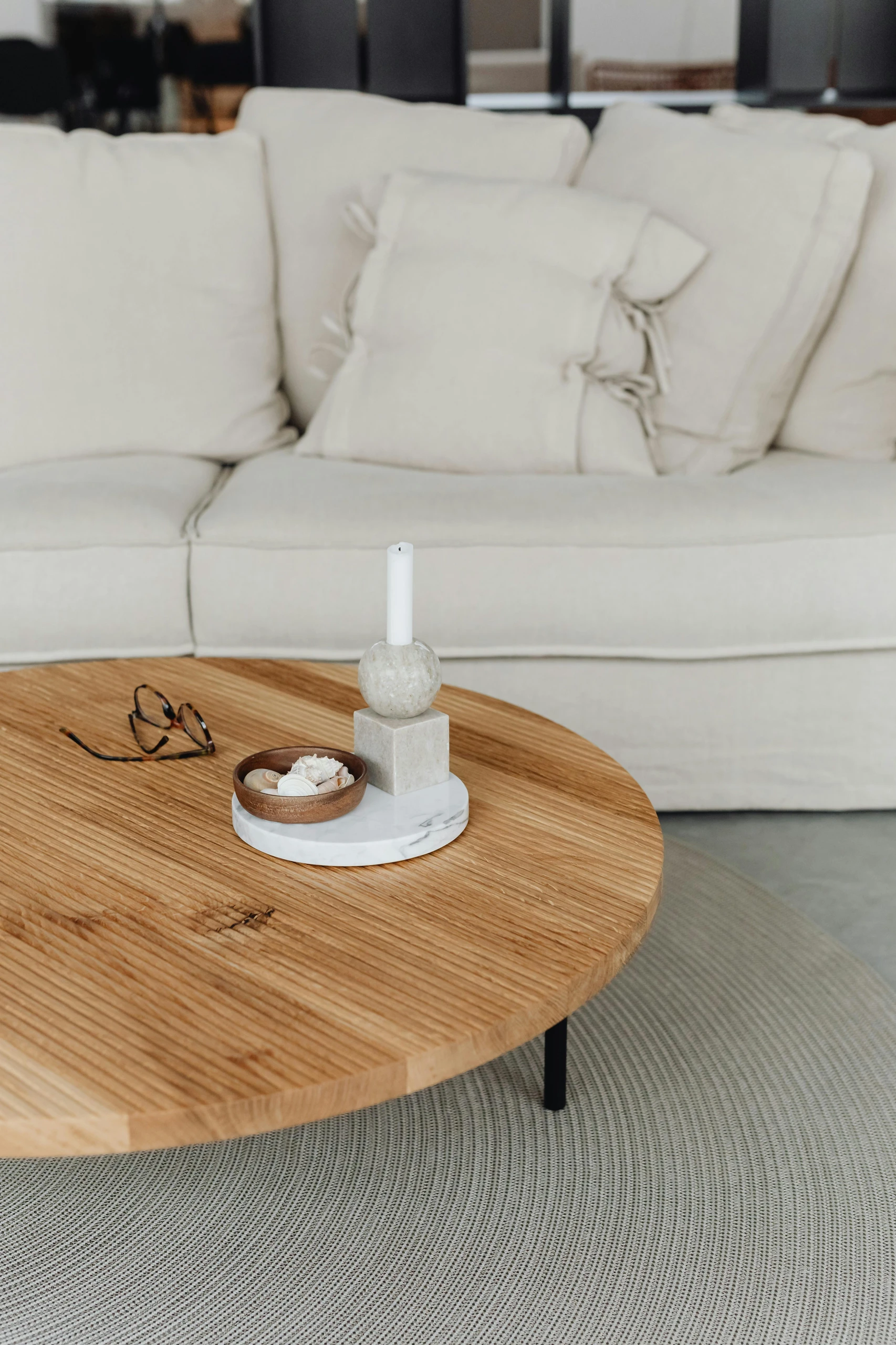 Modern inspiration for how to decorate a round coffee table featuring a minimalistic decor piece with candle, set on a marble tray alongside a small wooden bowl of natural elements, creating a clean and calming aesthetic.