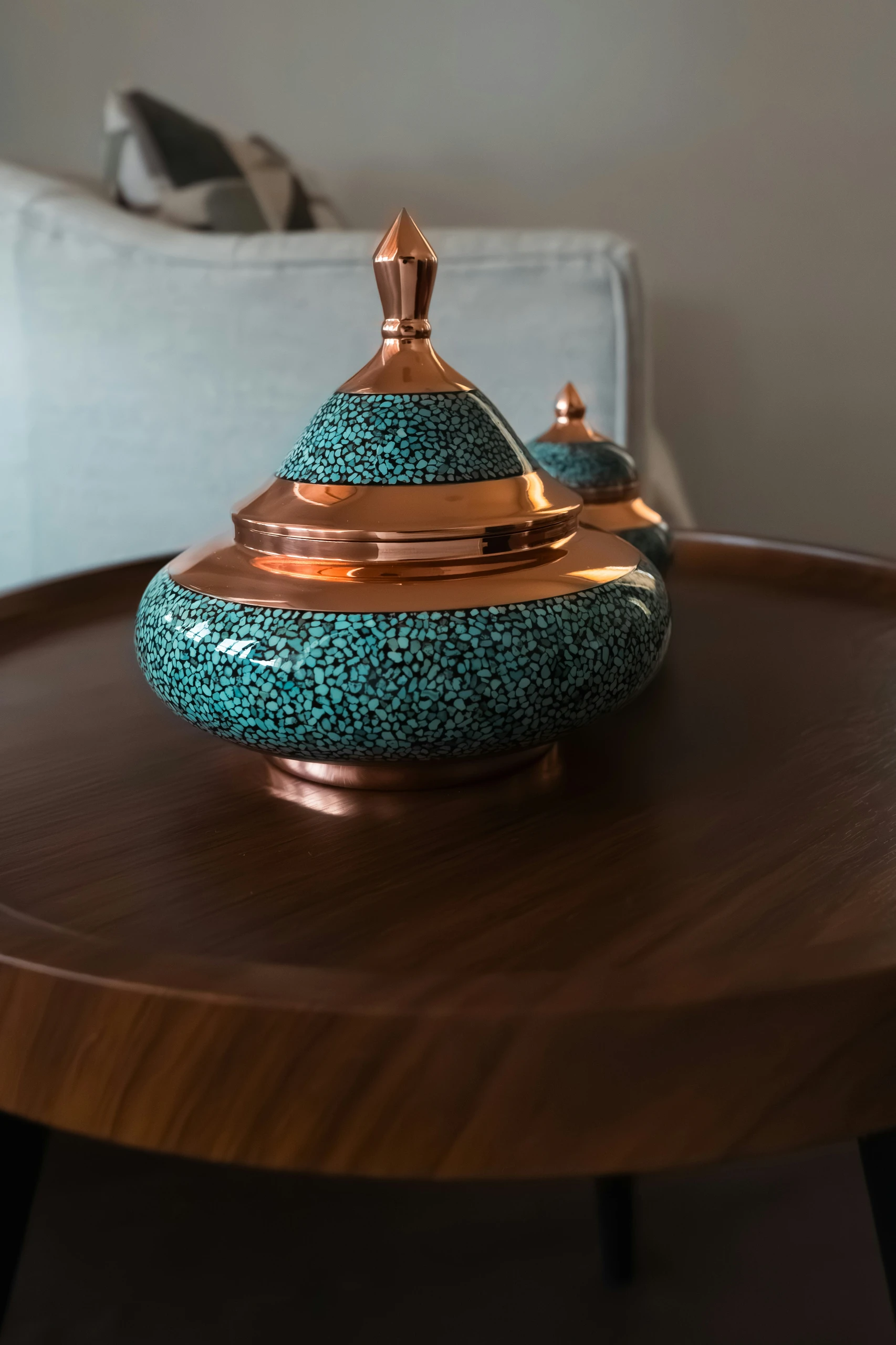 A versatile idea for how to decorate a round coffee table using a beautifully crafted porcelain box with turquoise mosaic details and copper accents. This elegant decorative piece adds a touch of cultural flair and works well in both traditional and contemporary interiors.