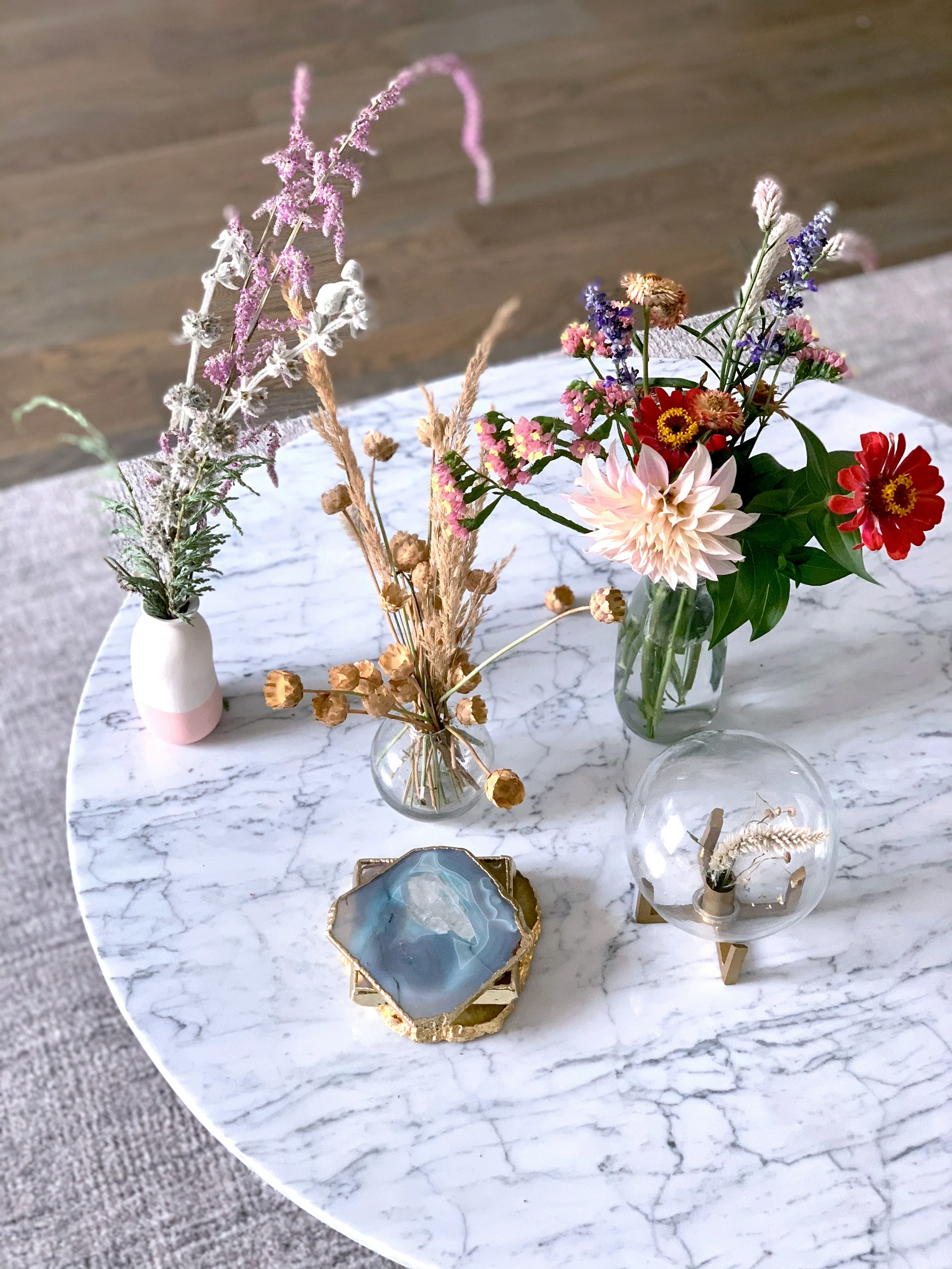 A stylish example of how to decorate a round coffee table using small vases with fresh and dried flowers, combining natural textures and soft colors for a versatile and seasonally adaptable centerpiece. The white marble table surface enhances the mix of floral arrangements and decorative accents, making it suitable for both minimalist and eclectic interiors.