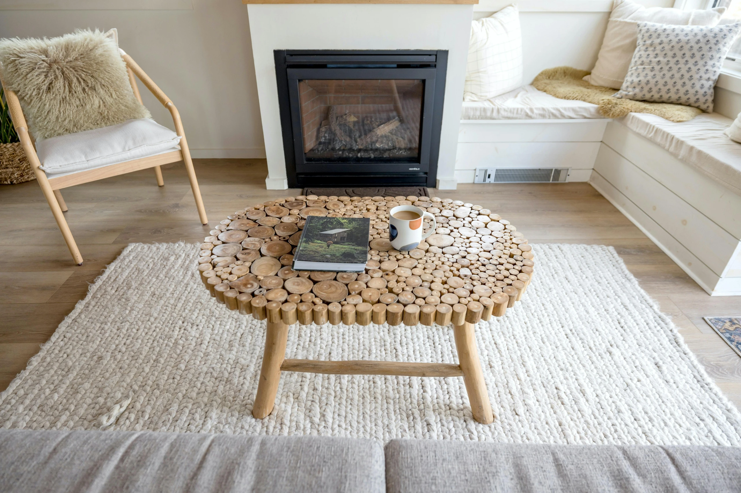 Cozy living room showcasing how to decorate a round coffee table with an unusual and natural round coffee table design made of wooden slices. The table features a simple yet inviting setup with a book and a coffee mug, demonstrating a versatile and earthy approach to table styling that complements minimalist or rustic interiors.