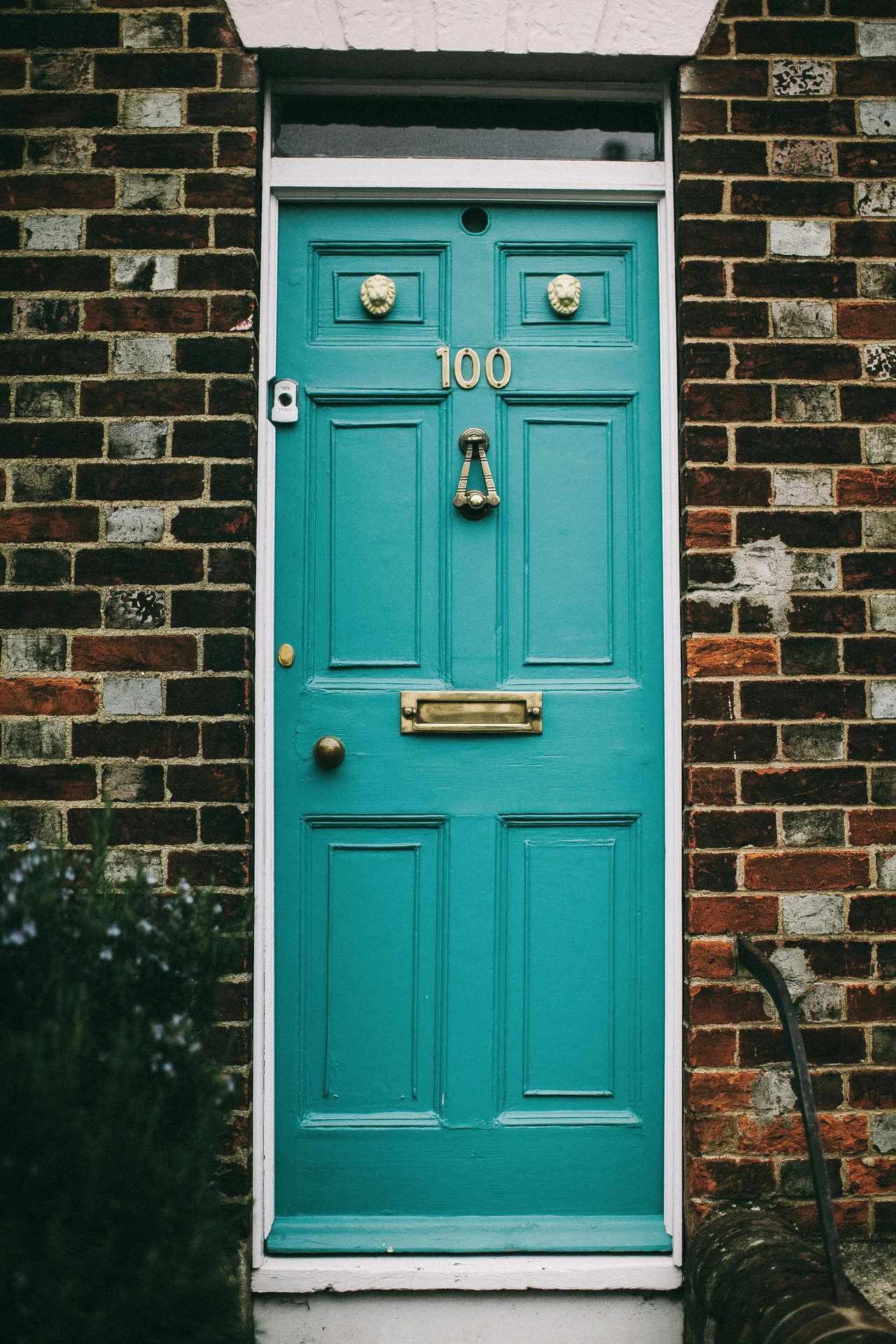 Bright turquoise front door with brass accents and house number 
