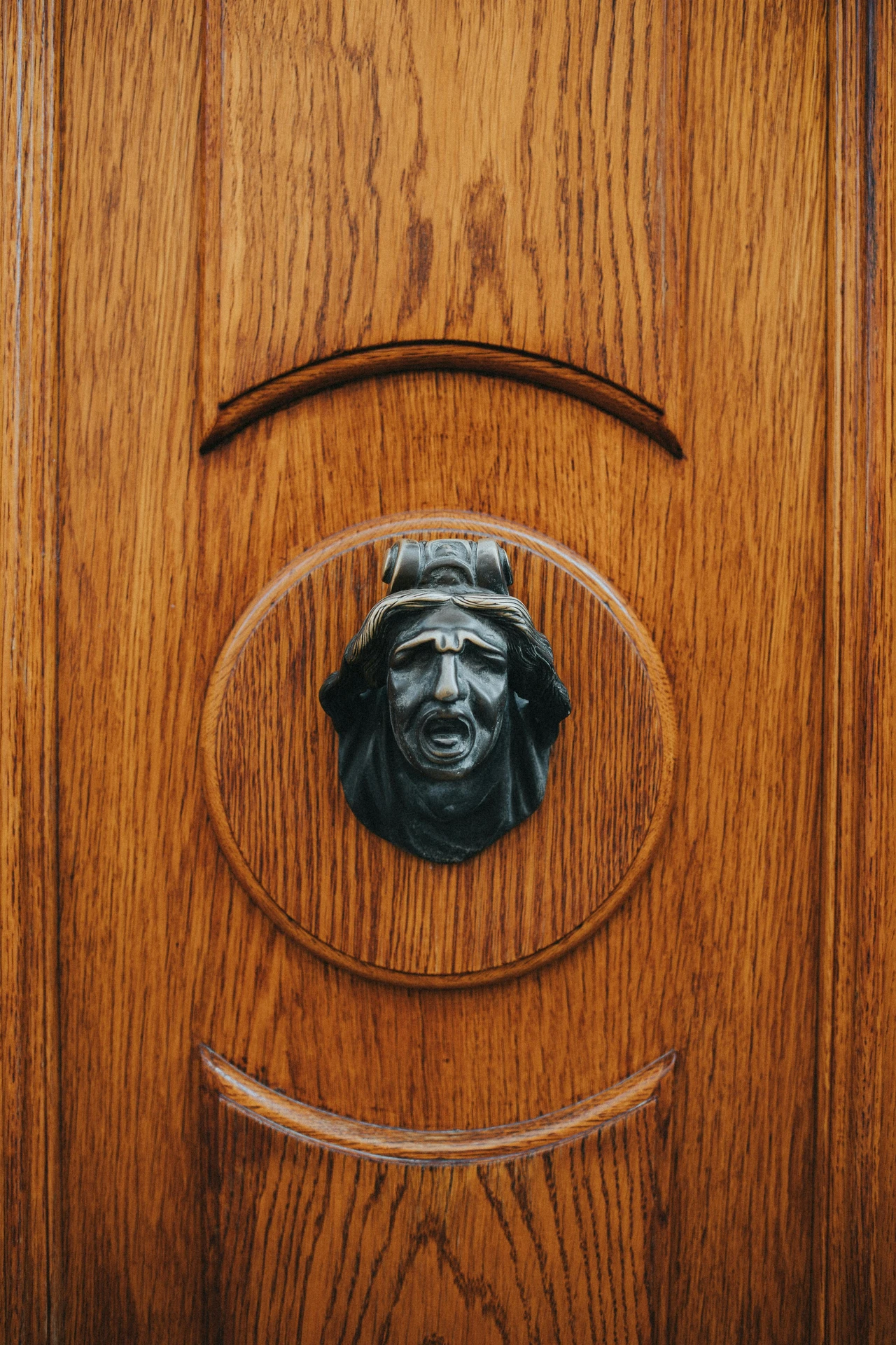 Close-up of a richly grained wooden front door featuring an antique, eye-catching hand knob shaped like a dramatic human face. A striking example of ideas for front door decor that adds personality and historic charm through a unique design element.