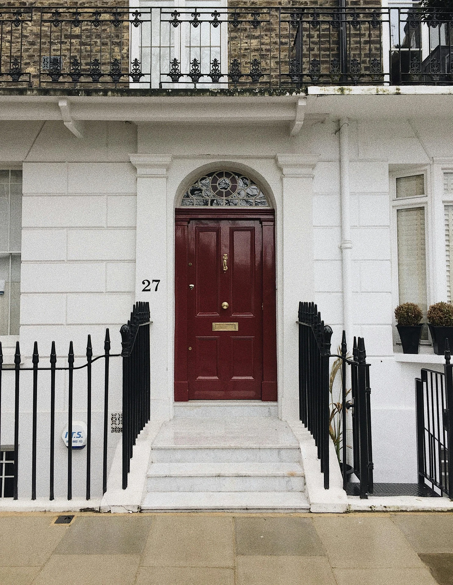 Elegant red front door framed by white pillars and a semicircular stained glass window, featuring gold hardware for a polished touch. An excellent example of ideas for front door decor embracing modern minimalism with classic London charm.