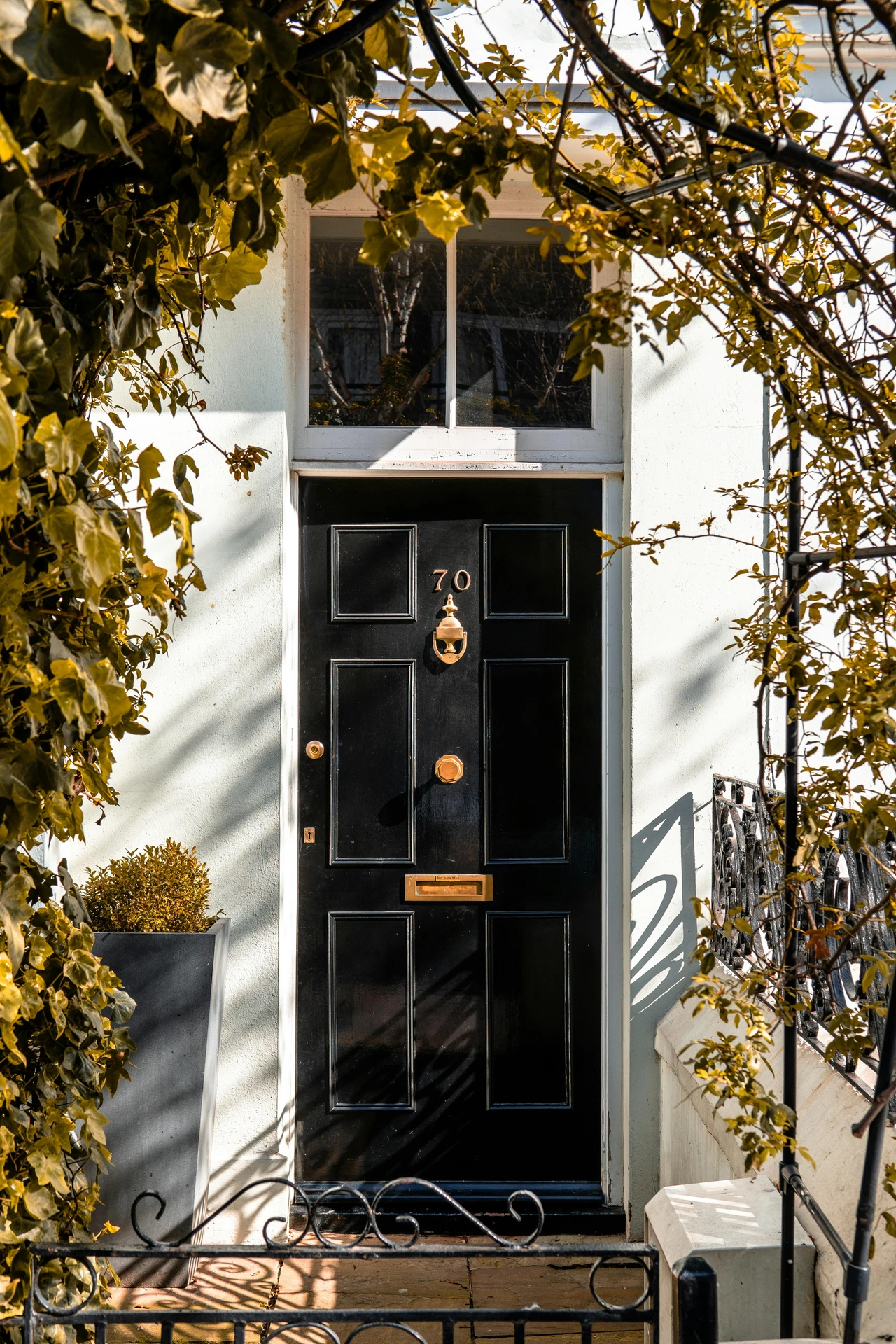 Elegant black front door framed by lush greenery and adorned with vintage gold hardware, offering timeless inspiration for those seeking ideas for front door decor with a sophisticated and classic touch.