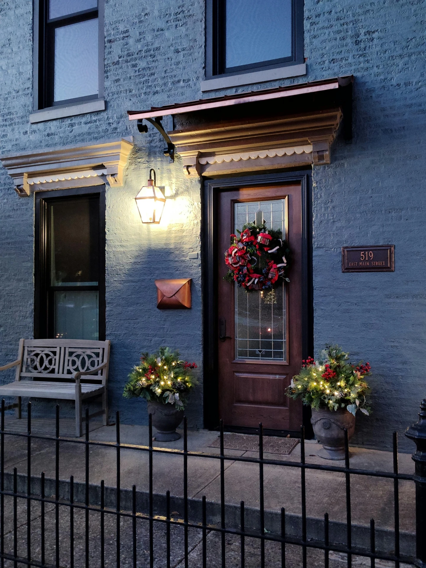 Charming evening view of a front door decorated with festive greenery, a seasonal wreath, and a glowing hanging lantern. Perfect inspiration for ideas for front door decor that combine cozy lighting and classic elements for a welcoming holiday look.
