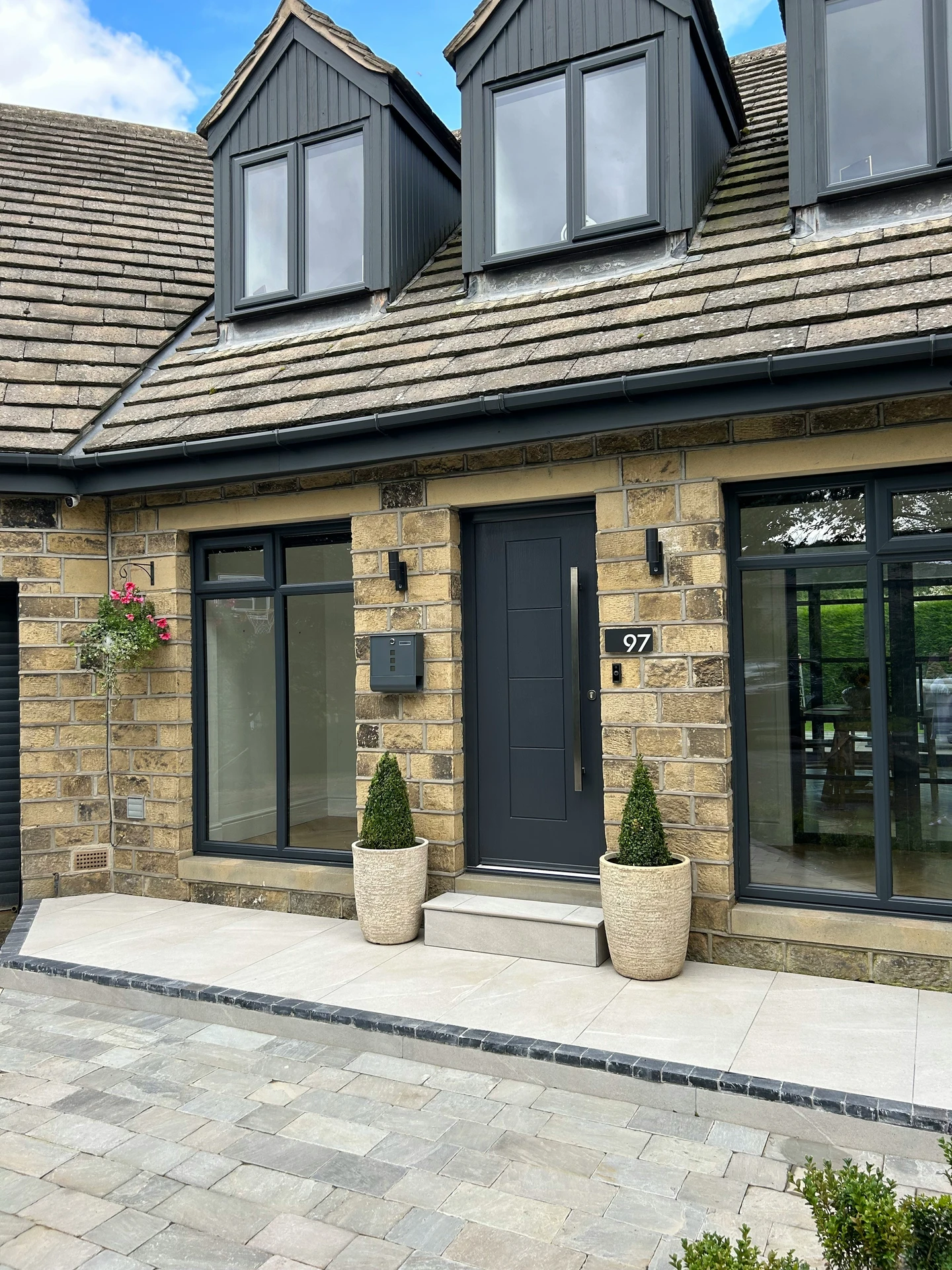Modern stone house exterior featuring a sleek matte black door with a minimalist matte black door handle, flanked by matching windows and two tall potted topiaries, offering versatile ideas for front door decor that combine clean lines with contemporary curb appeal.