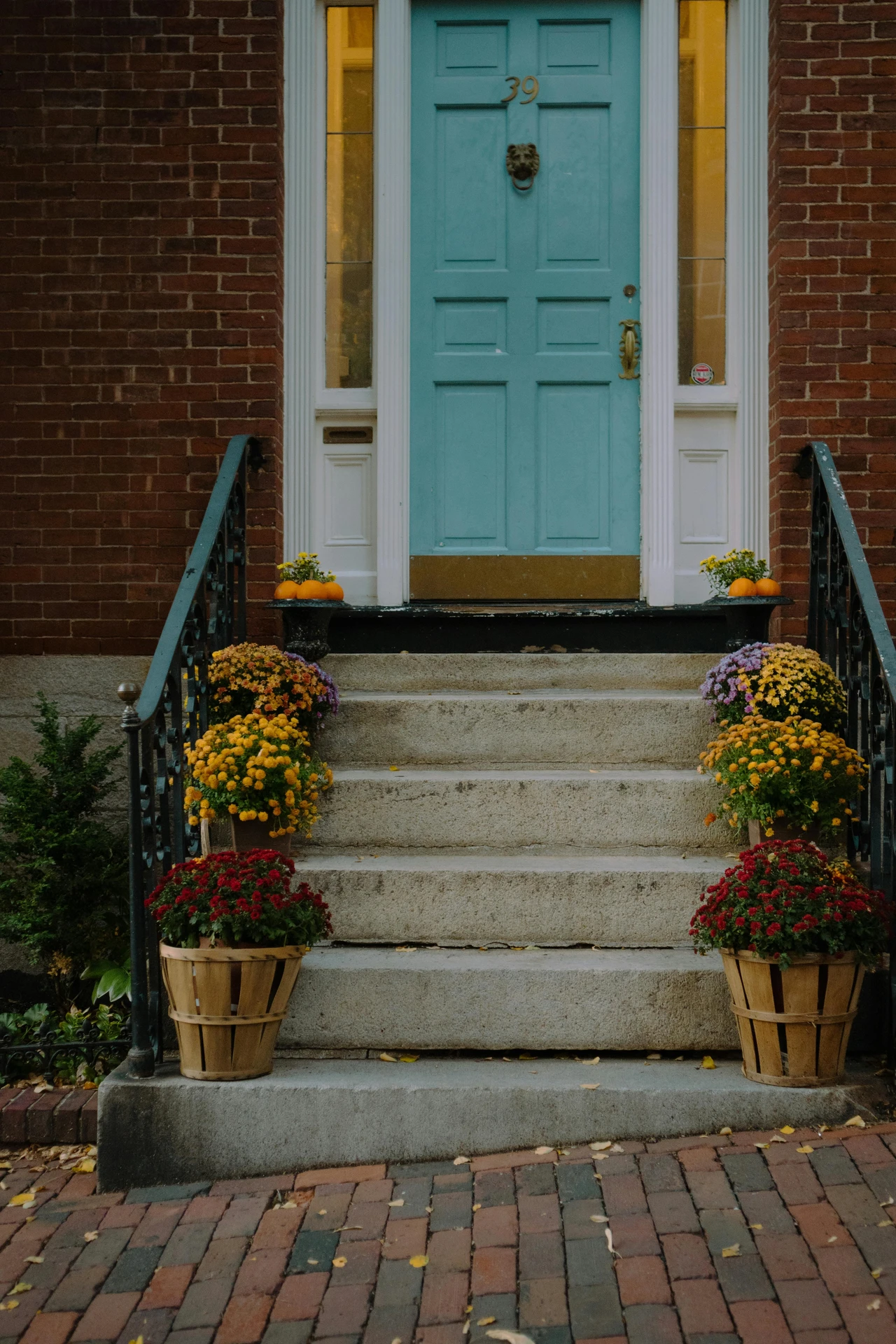 Charming entryway featuring a teal door framed by sidelights, with steps lined by multiple flower pots filled with vibrant autumn blooms in red, yellow, and purple, an inspiration for ideas for front door decor that use multiple flower pots to create a warm, seasonal welcome.