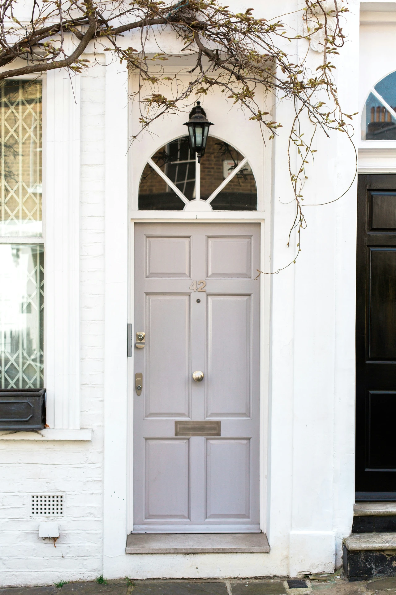 Soft lilac front door with elegant silver hardware and classic paneling, framed by a white archway and topped with a decorative transom window. An inspiring example of ideas for front door decor that blend charm and versatility with refined silver accents.