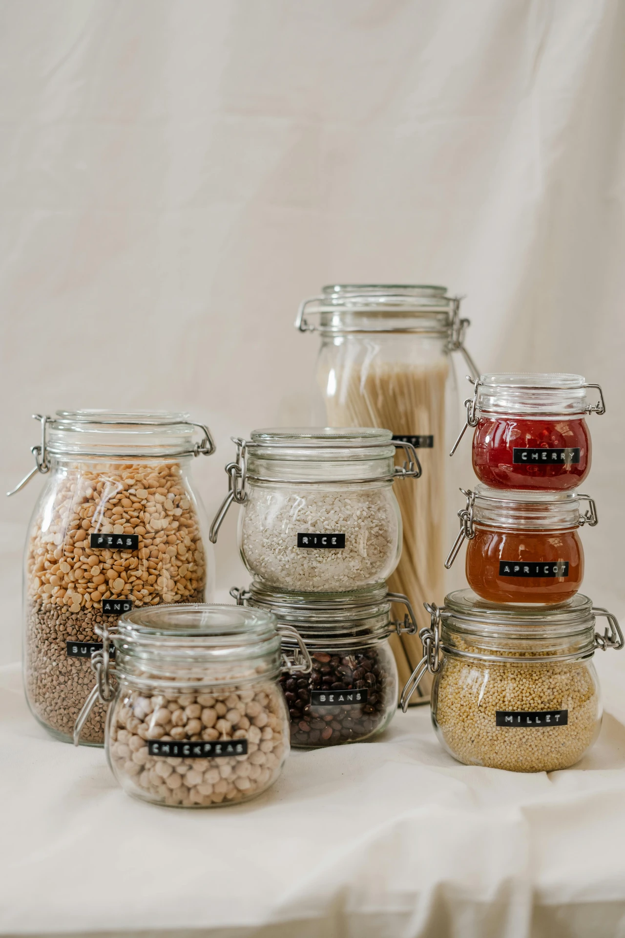 Neatly arranged set of labeled glass jars filled with pantry staples like rice, beans, chickpeas, pasta, and jam, offering practical and aesthetic kitchen island decor ideas. The glass containers on kitchen island surfaces create an organized, clean look while keeping essentials easily accessible, perfect for a cozy and functional kitchen design.