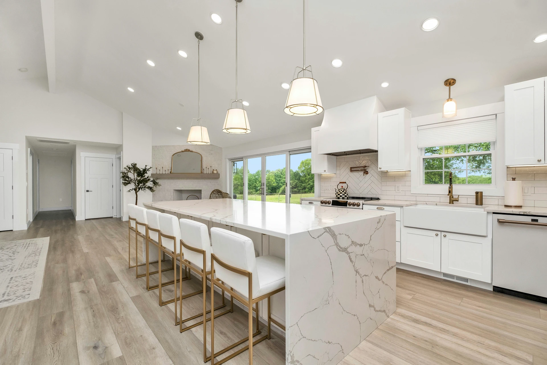 Spacious and elegant kitchen featuring a large waterfall-edge marble island that serves as the focal point of the room. Surrounded by sleek white cabinetry, gold-accented bar stools, and warm pendant lighting, the space offers inspiration for luxurious kitchen island decor ideas. The marble island enhances the clean, bright aesthetic while providing ample space for dining and entertaining.