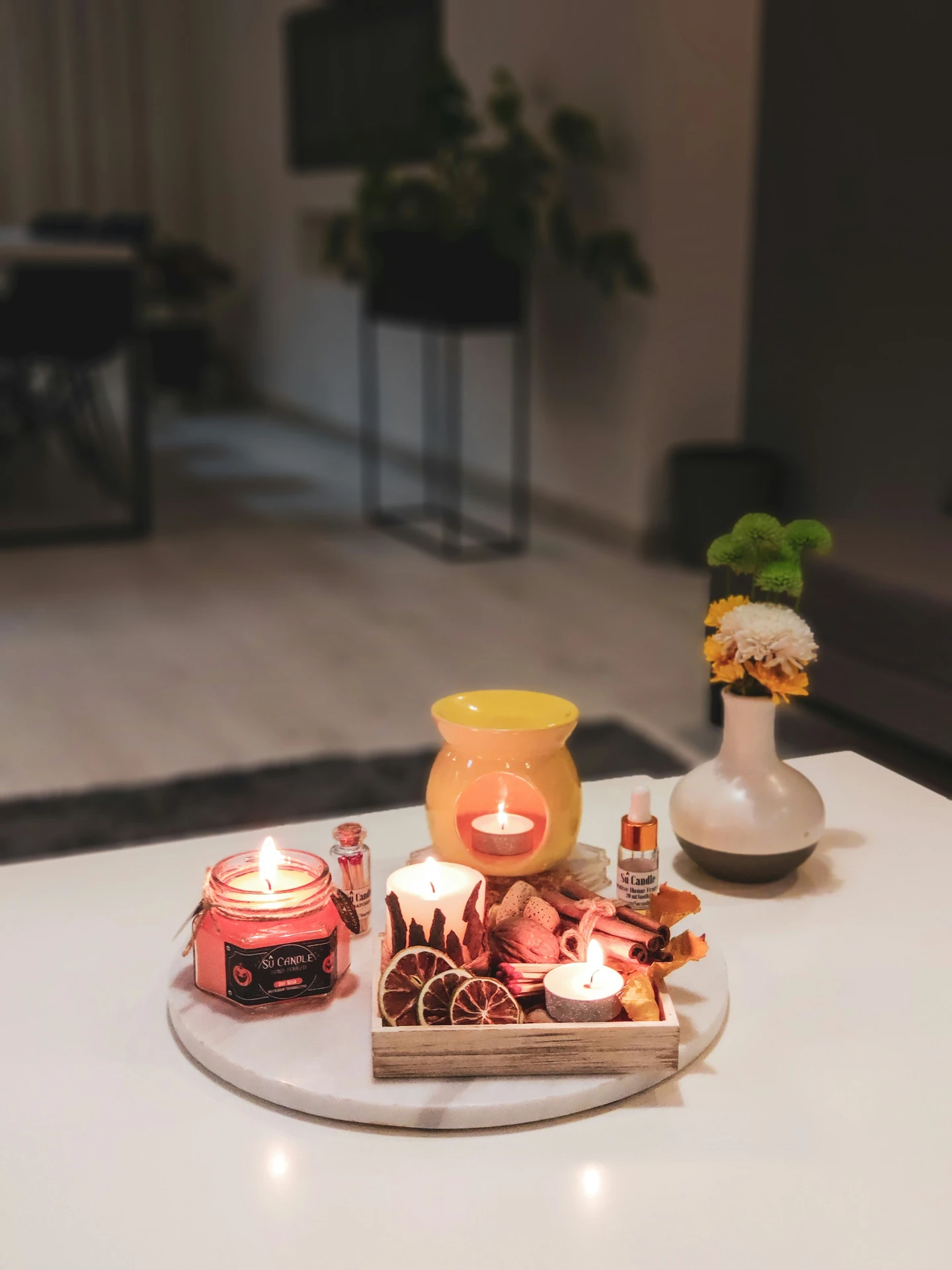 Cozy and inviting tabletop scene featuring a round tray with lit candles, dried citrus, cinnamon sticks, and a yellow wax warmer, complemented by a small vase of flowers. This arrangement showcases warm kitchen island decor ideas with a touch of seasonal decor, perfect for creating an autumnal or festive atmosphere in any modern home.