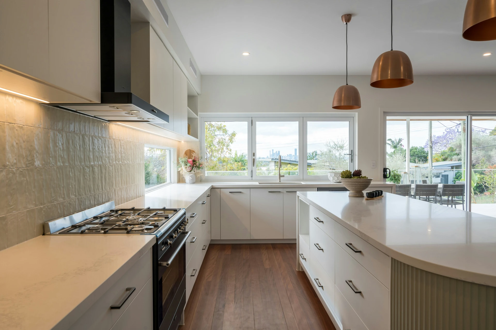 Modern and airy kitchen with a large central island showcasing elegant kitchen island decor ideas, including a textured ceramic bowl with succulents. The island features ample drawers and cabinetry, offering practical smart storage solutions that enhance both functionality and aesthetics. Copper pendant lights and panoramic windows add warmth and brightness to the clean, minimalist design.