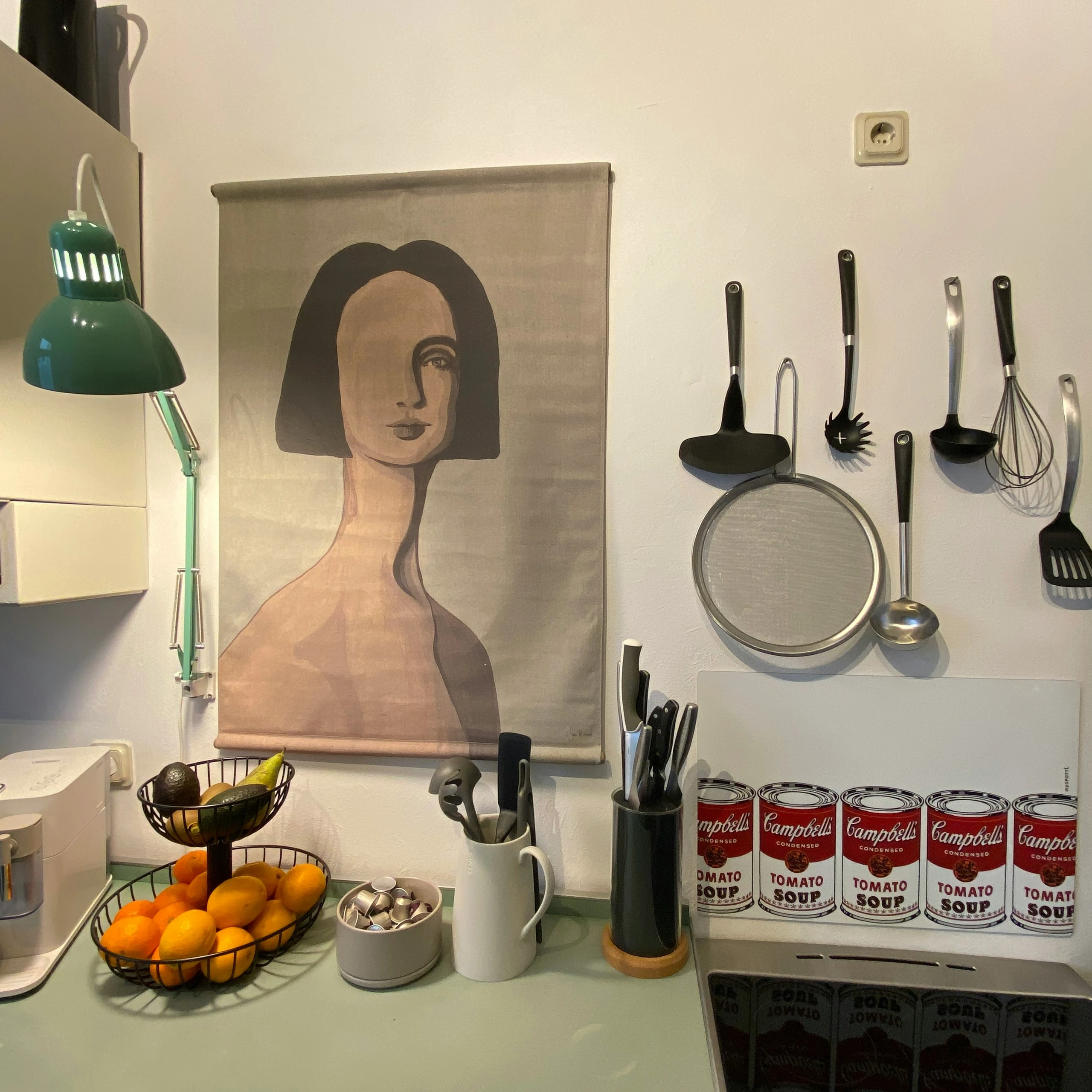 Cozy kitchen corner featuring small kitchen decor ideas with a personal touch, including wall art, a green desk lamp, Warhol-style soup can prints, and a mix of practical and decorative kitchen tools.