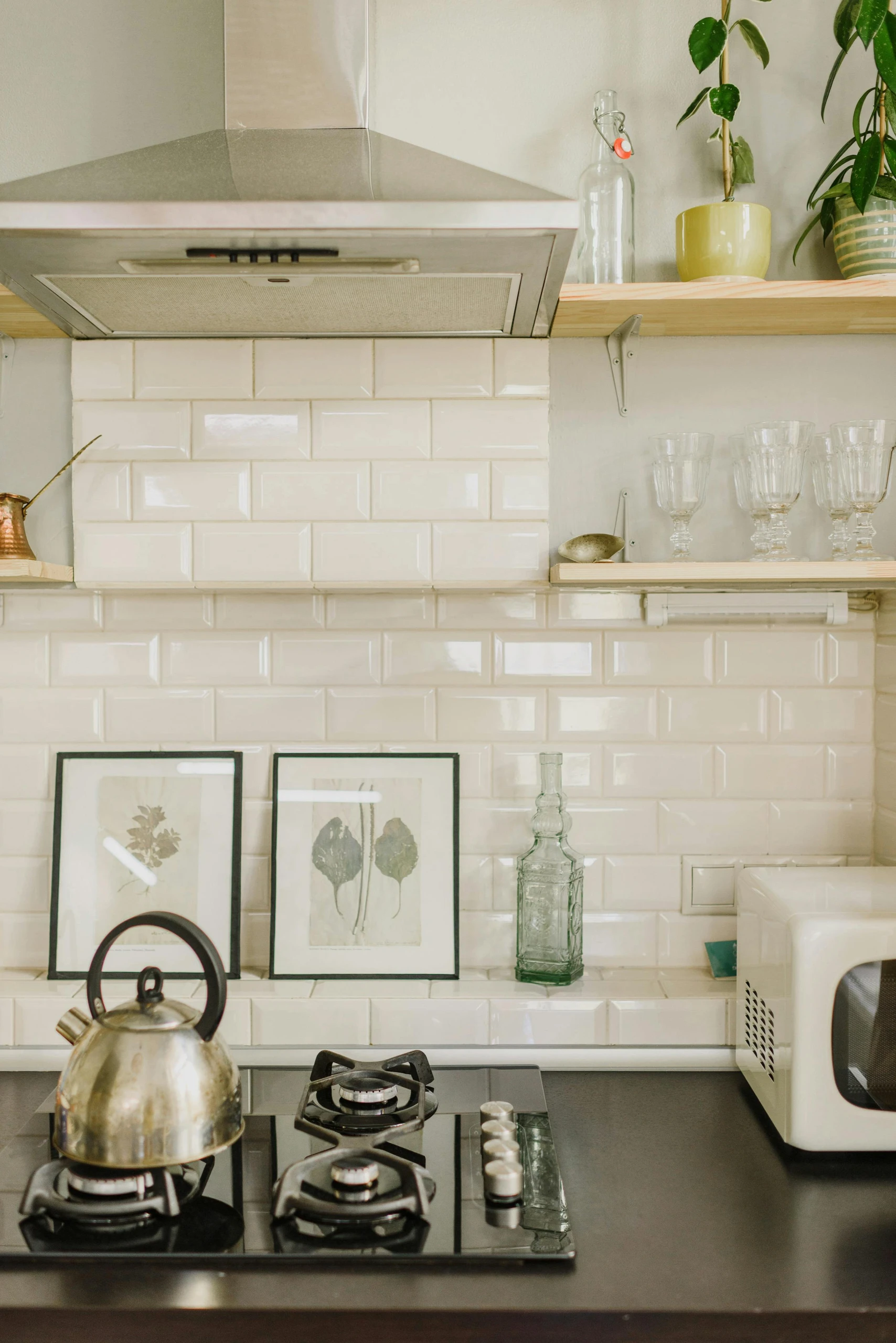 Cozy kitchen showcasing small kitchen decor ideas with charming pretty backsplash tiles, open shelves with plants and glassware, and a vintage touch through framed prints and a classic kettle.