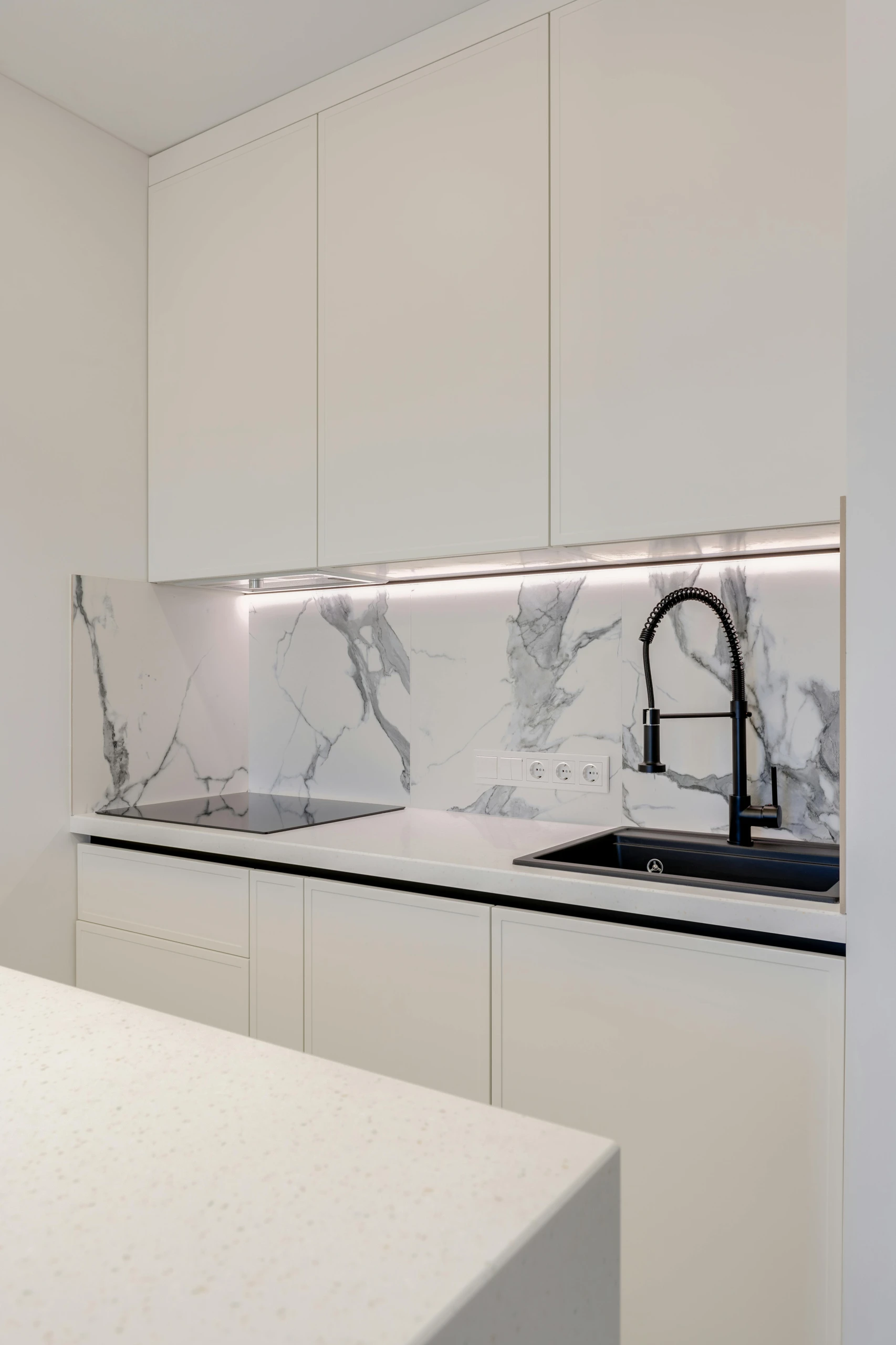 Modern white kitchen with marble backsplash and sleek black faucet, showcasing small kitchen decor ideas with elegant under cabinet lighting for a bright and stylish workspace.