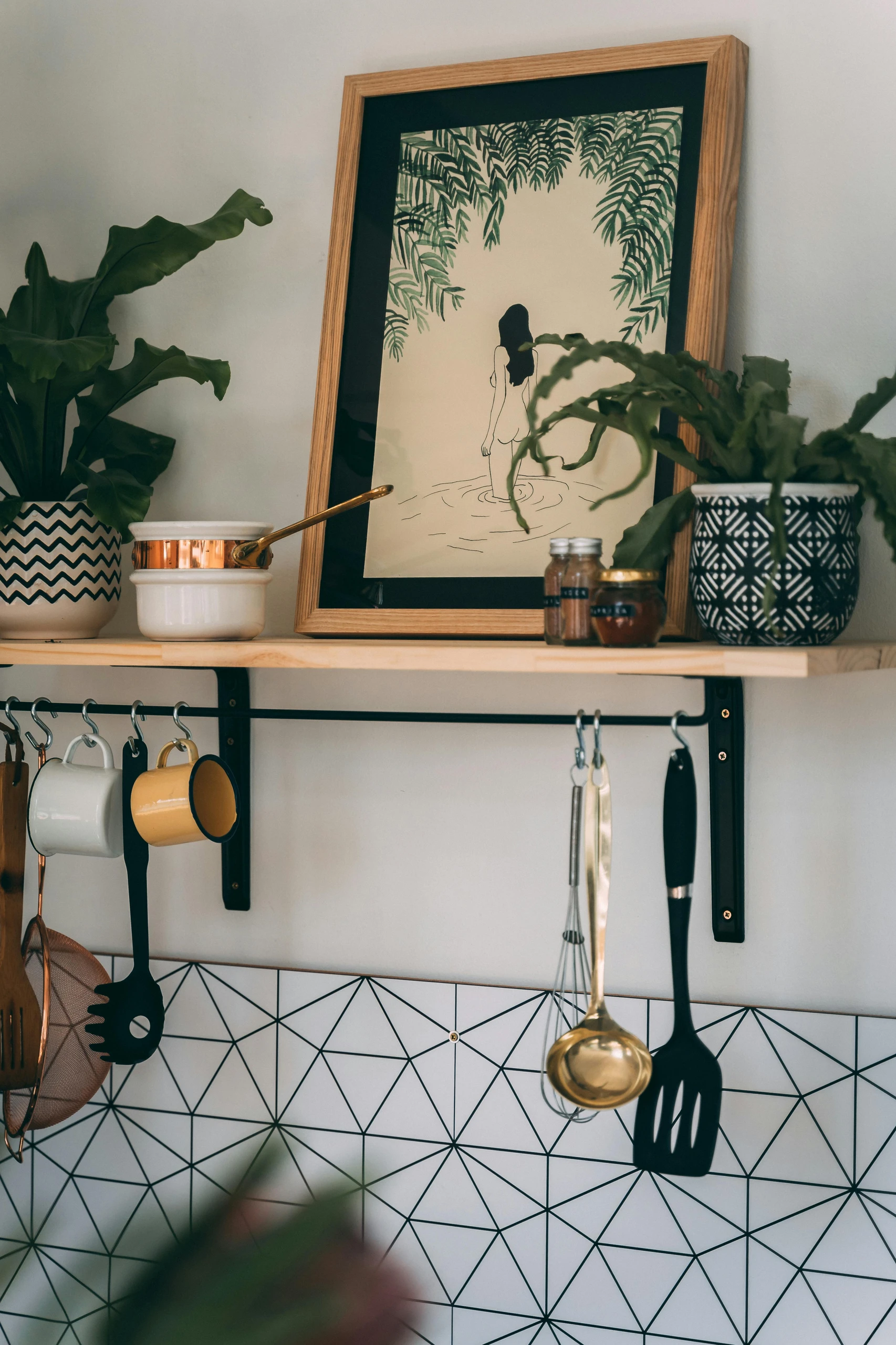 Stylish kitchen corner showcasing small kitchen decor ideas, featuring framed art, patterned planters, and clever hooks to utilize the space under the shelf for hanging mugs and utensils.