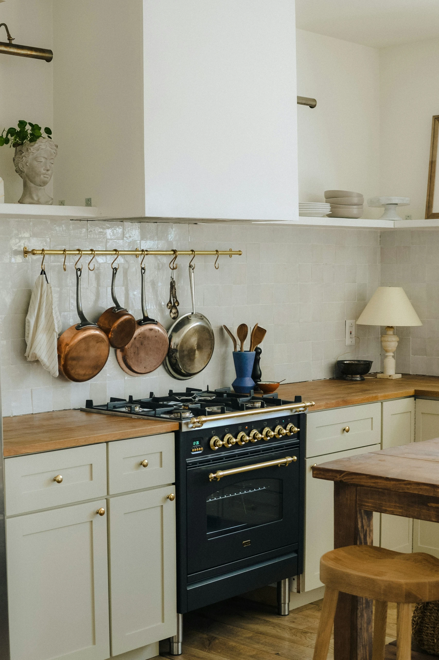 Stylish kitchen corner showcasing a wall-mounted pot rack with hanging copper pans above a vintage stove. One of the best small kitchen decor ideas for combining function with elegant, space-saving design.