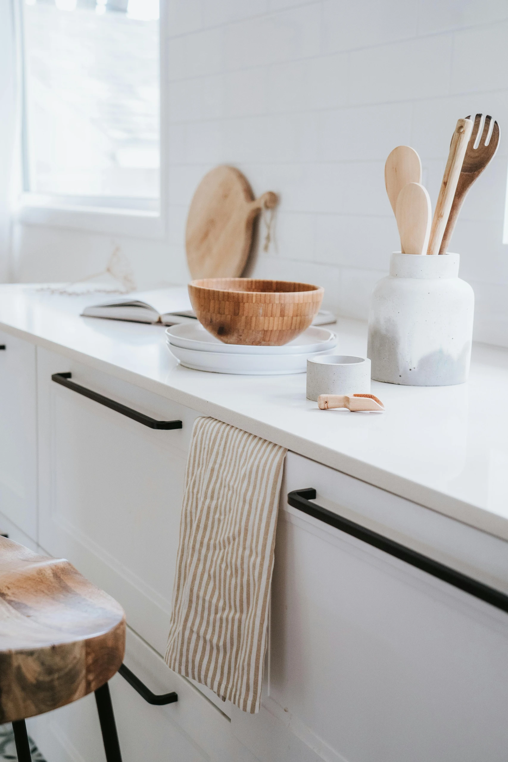 Minimalist countertop showcasing small kitchen decor ideas with natural wood elements, including a wooden bowl, utensils, and stool, all complemented by neutral tones and soft lighting.