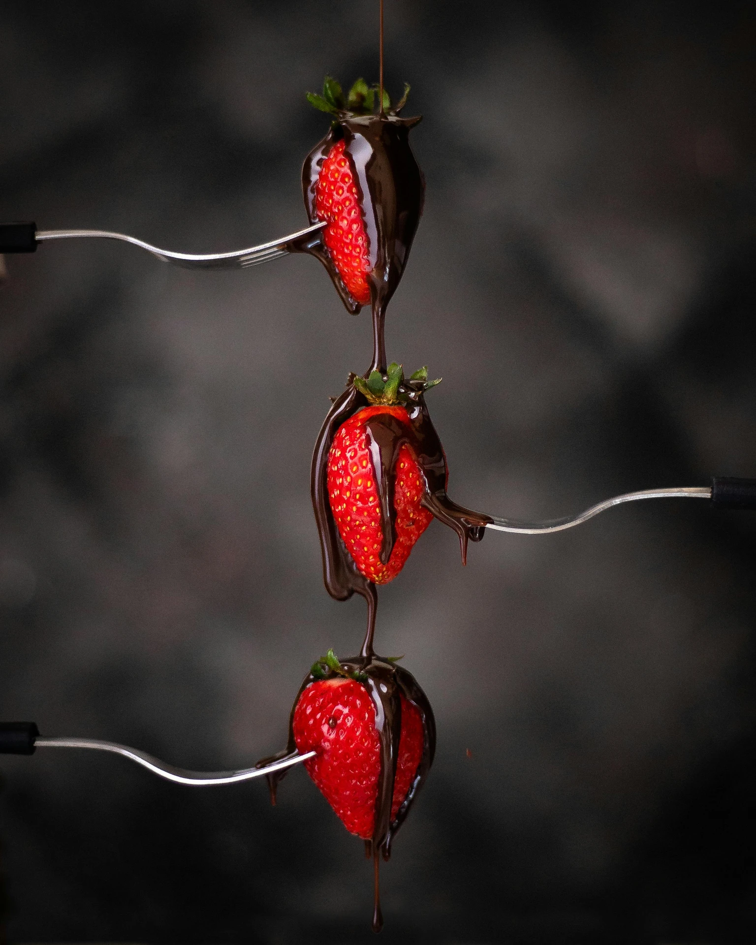 Fresh strawberries elegantly skewered on forks are being drizzled with rich, melted chocolate from a chocolate fountain, highlighting the indulgent side of small kitchen appliances. The glossy dark chocolate cascades over the vibrant red berries, creating a visually tempting treat perfect for parties, romantic desserts, or creative plating ideas.