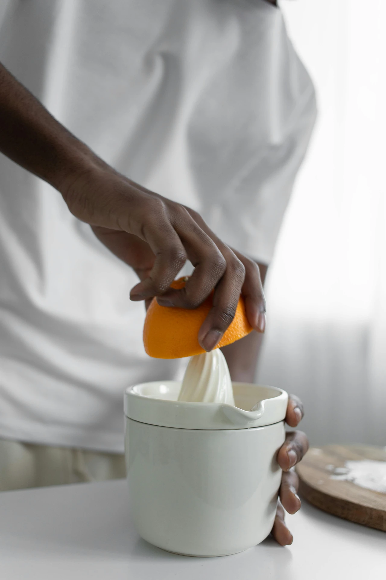 A person presses half an orange onto a manual lemon squeezer, demonstrating how small kitchen appliances can make preparing fresh juice quick and effortless. The white squeezer sits on a countertop, ready to capture every drop, making it ideal for citrus fruits like lemons, limes, and oranges in both everyday cooking and refreshing beverage recipes.