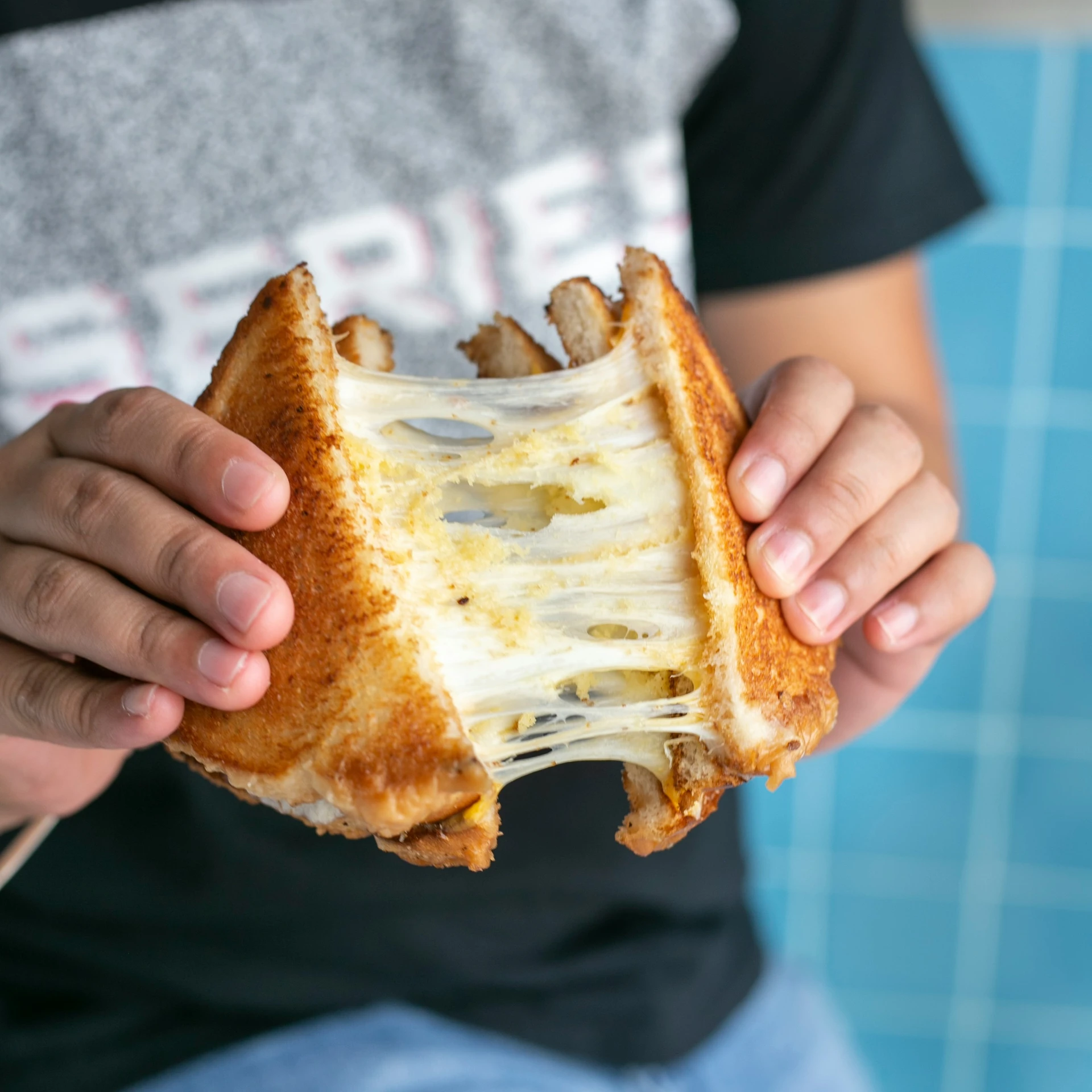 Close-up of a person pulling apart a golden, crispy grilled cheese sandwich with perfectly melted, stretchy cheese inside, made using a sandwich maker. This tasty creation highlights how small kitchen appliances can quickly prepare versatile snacks, from classic comfort food to creative gourmet combinations.