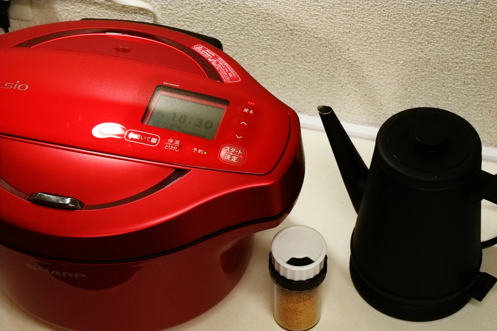 Red digital slow cooker on a kitchen counter beside a sleek black electric kettle and a small spice jar, illustrating how small kitchen appliances like a slow cooker can simplify preparing everything from hearty stews to tender roasts with minimal effort.