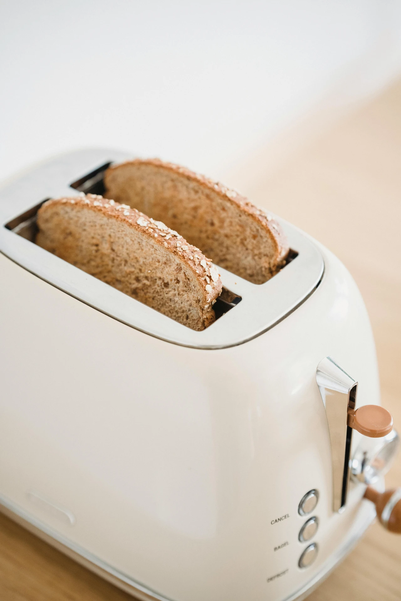 Close-up of a modern cream-colored toaster with two slices of whole grain bread toasting, showcasing how small kitchen appliances like a toaster can quickly prepare anything from a simple breakfast to gourmet toast creations with various toppings.