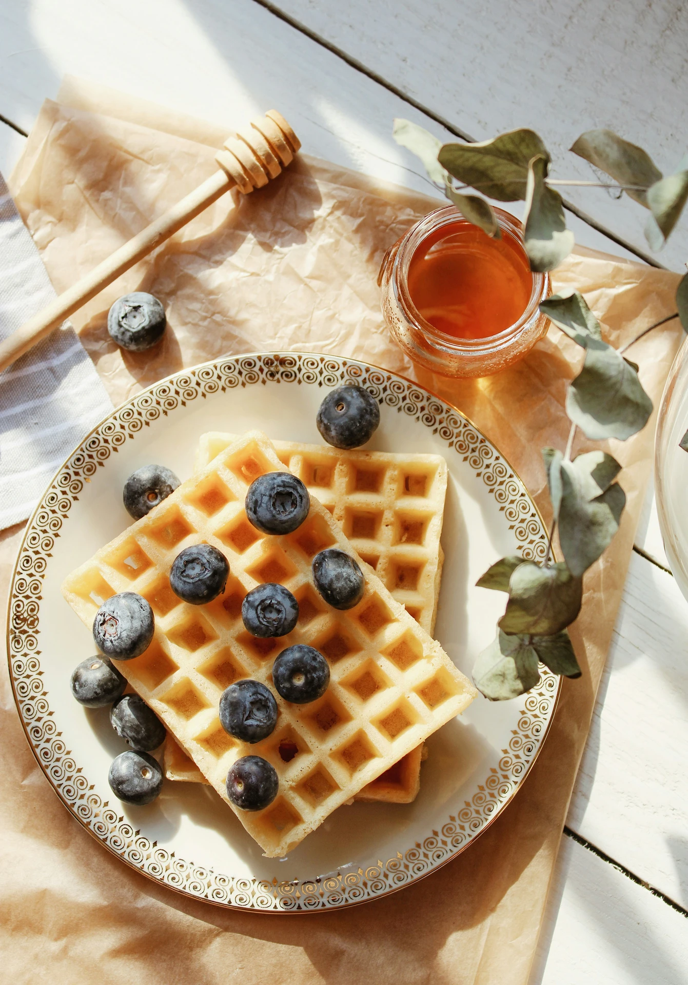 Golden, freshly made waffles topped with plump blueberries on an ornate plate, accompanied by a jar of honey and a wooden honey dipper, illustrating how small kitchen appliances like a waffle maker can create everything from sweet breakfast treats to savory snacks for any time of day.